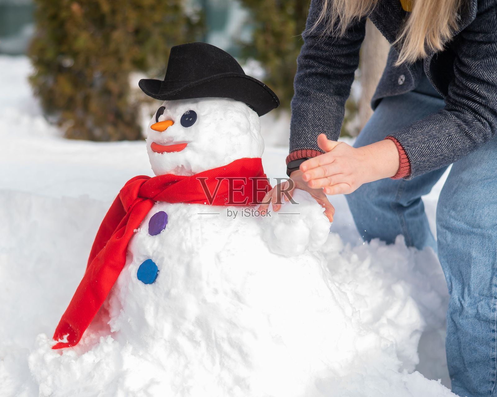一个白人妇女用雪雕刻雪人。胡萝卜是鼻子的位置。照片摄影图片