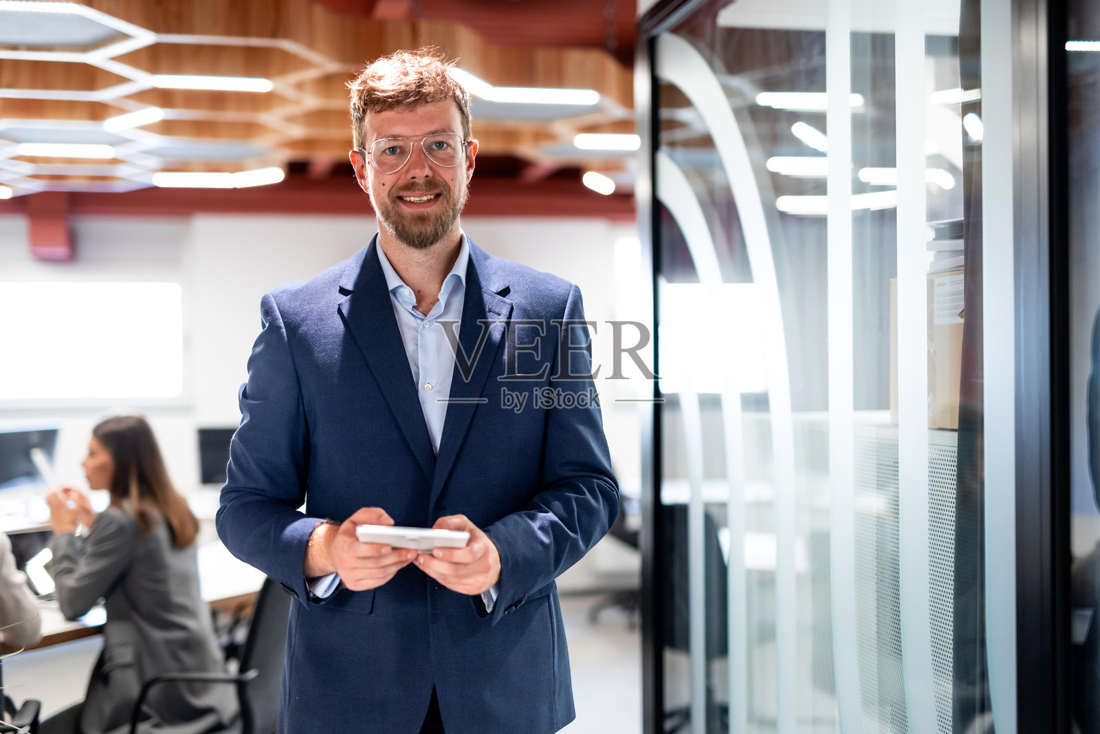 快乐的男性企业家使用数码平板电脑，微笑着站在现代化的办公室里照片摄影图片