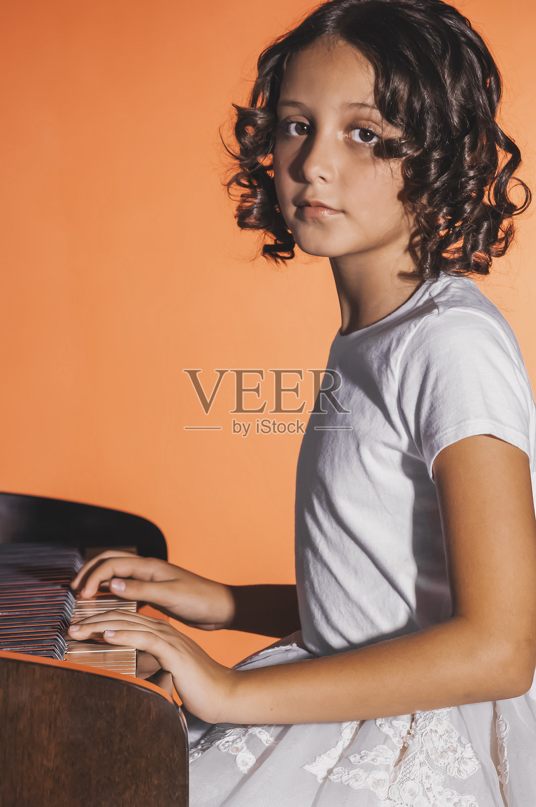 年轻女孩在橙色背景下弹钢琴照片摄影图片