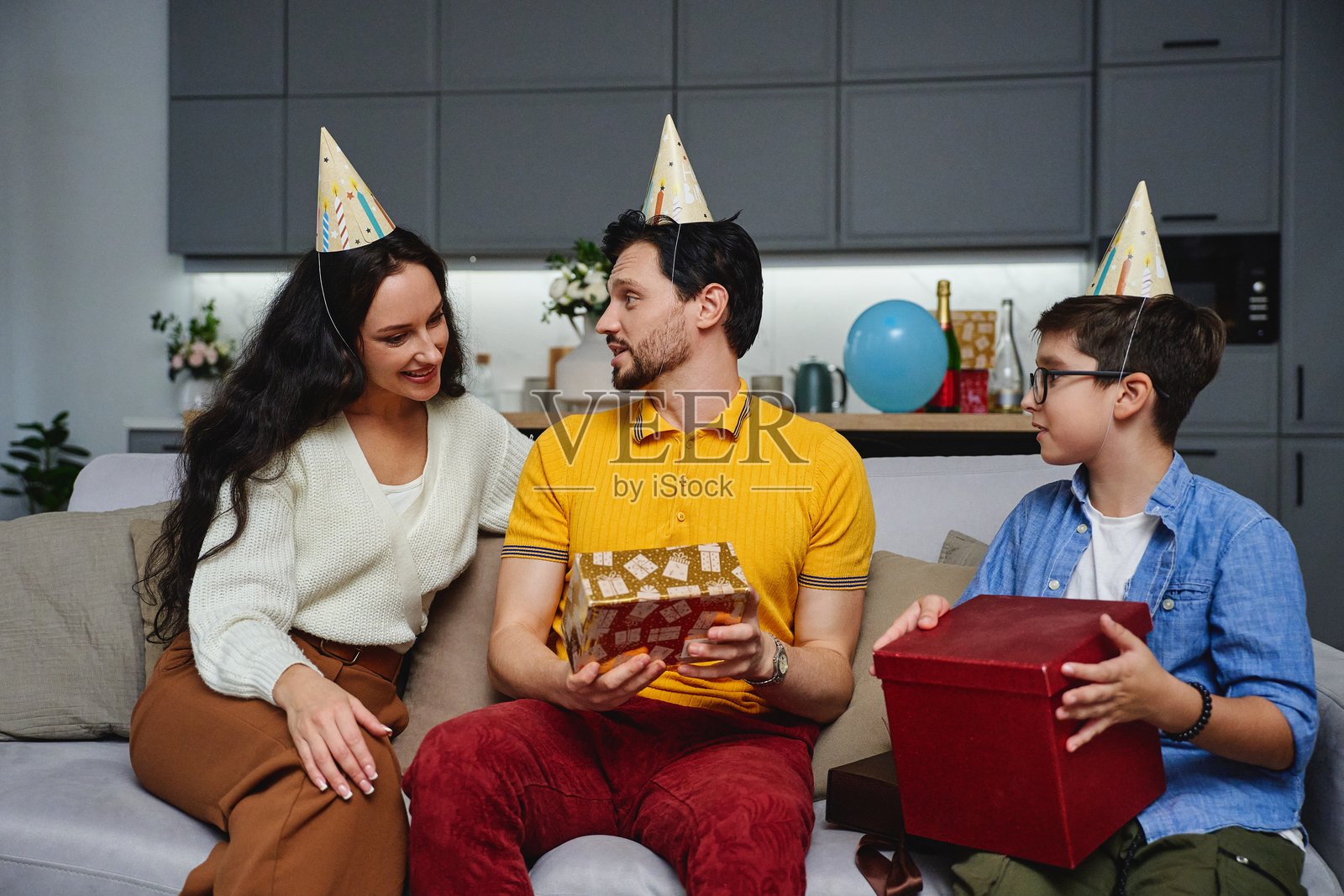 温馨的客厅里，家人庆祝生日，戴着生日帽，周围摆满了礼物。照片摄影图片