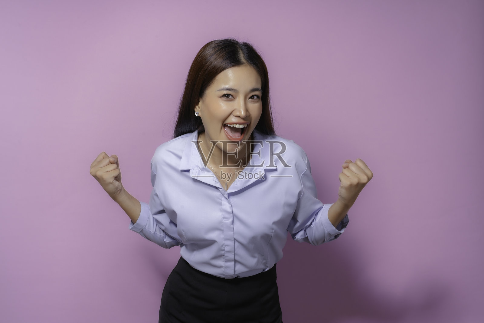 兴奋的亚洲女商人在粉红色的办公室背景中高举拳头庆祝成功。她积极的表情激发了胜利和动力照片摄影图片