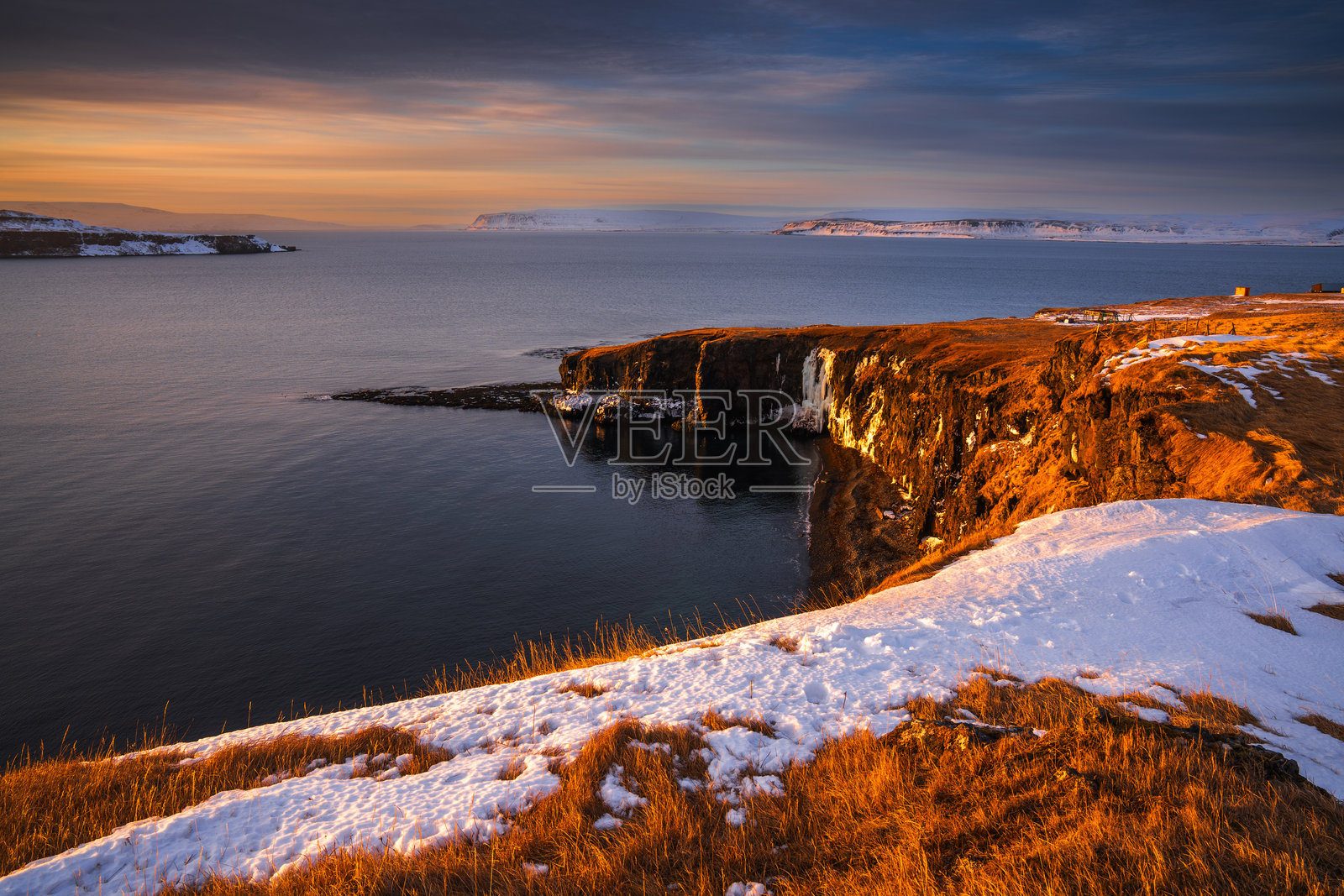 悬崖上覆盖着雪的海洋日落景色照片摄影图片