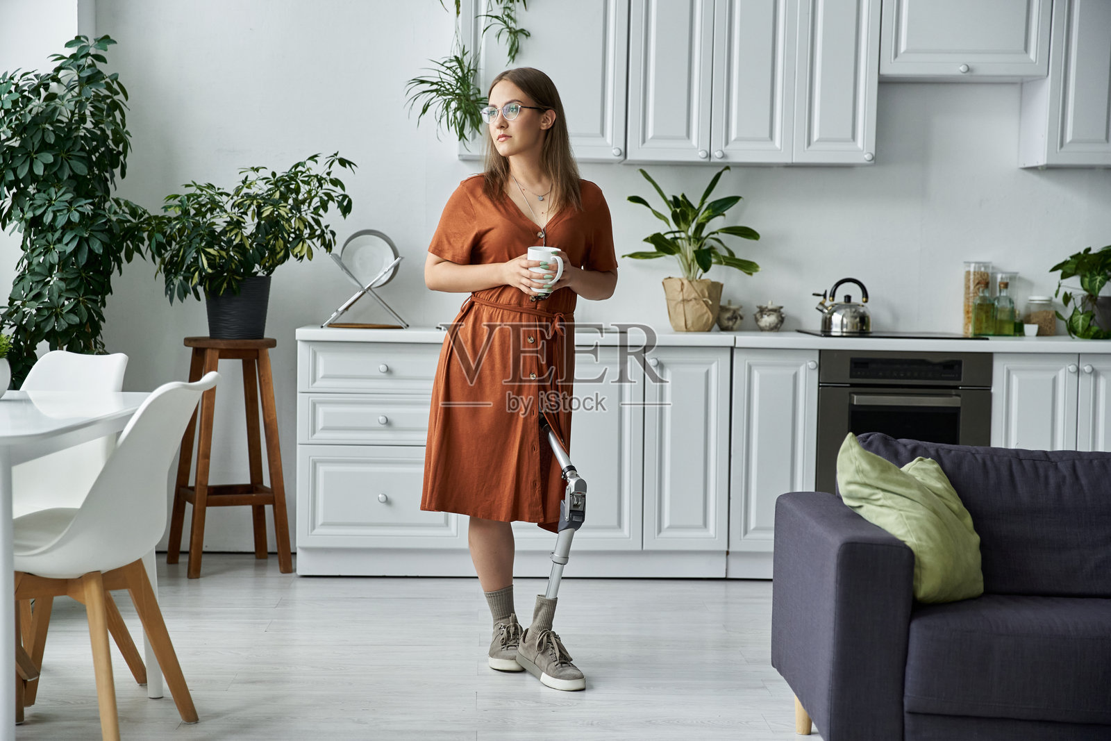 年轻女性在温馨现代的厨房里享受热饮，腿部有假肢。照片摄影图片