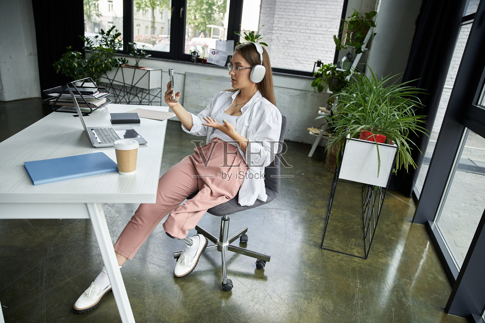 年轻女性在现代工作空间中参加虚拟会议，佩戴假肢。照片摄影图片