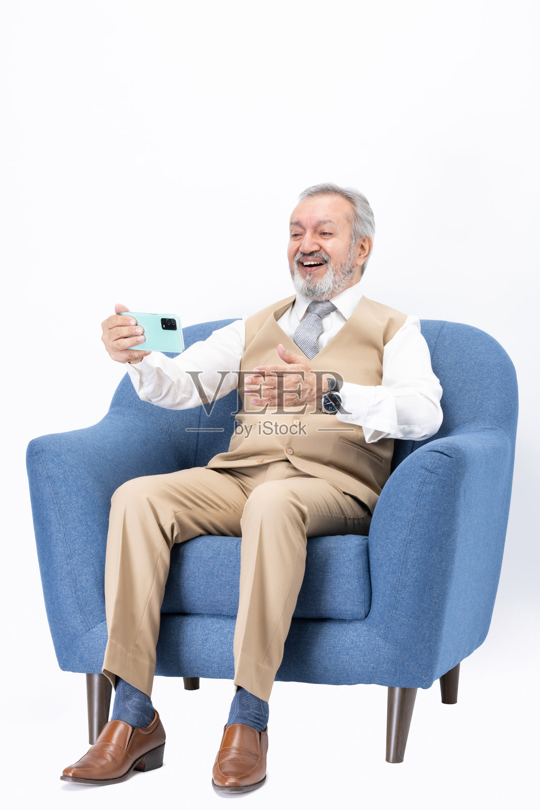 坐在沙发上使用手机的老年人，背景为白色。照片摄影图片