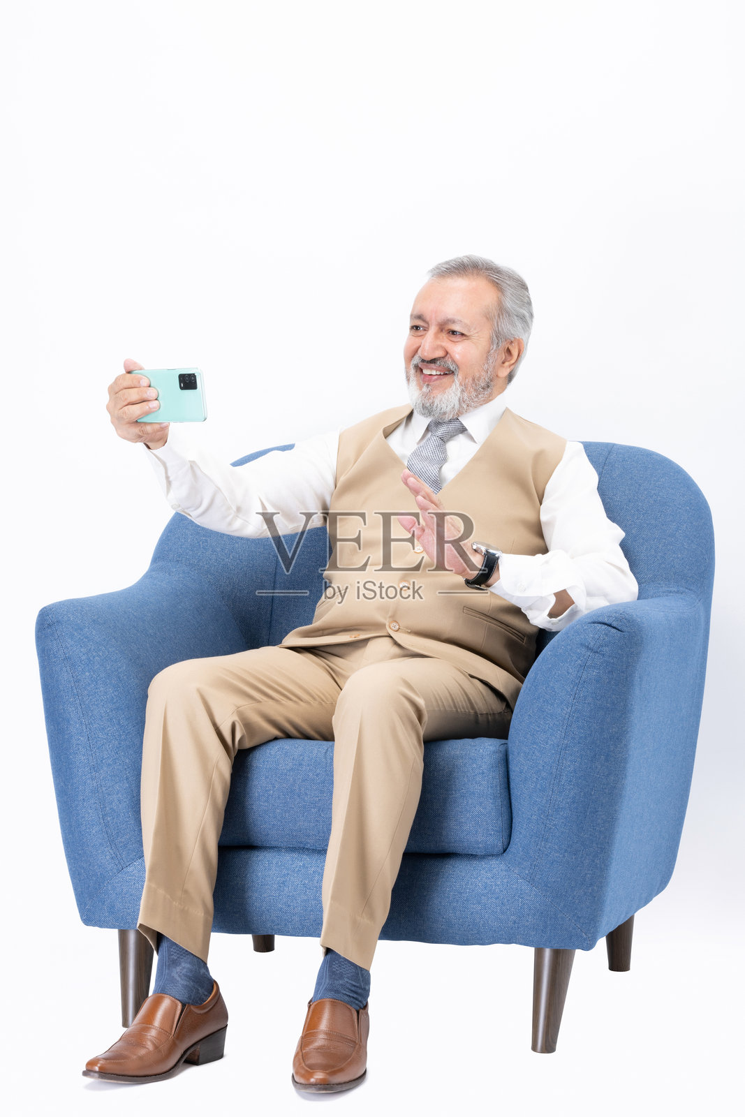 坐在沙发上使用手机的老年男性，背景为白色。照片摄影图片
