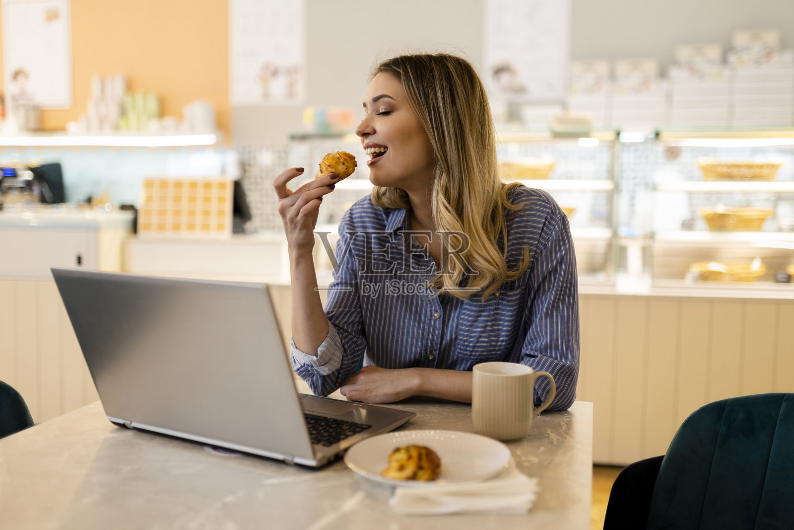 微笑的年轻女性坐在咖啡馆里，手里拿着咖啡杯，正在使用笔记本电脑工作。照片摄影图片