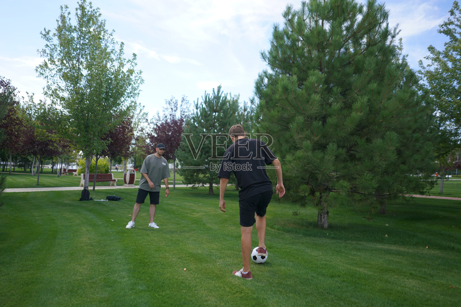 两名男子在友好的足球比赛中，熟练地在一片绿草如茵、树木环绕的场地上互相传球。照片摄影图片