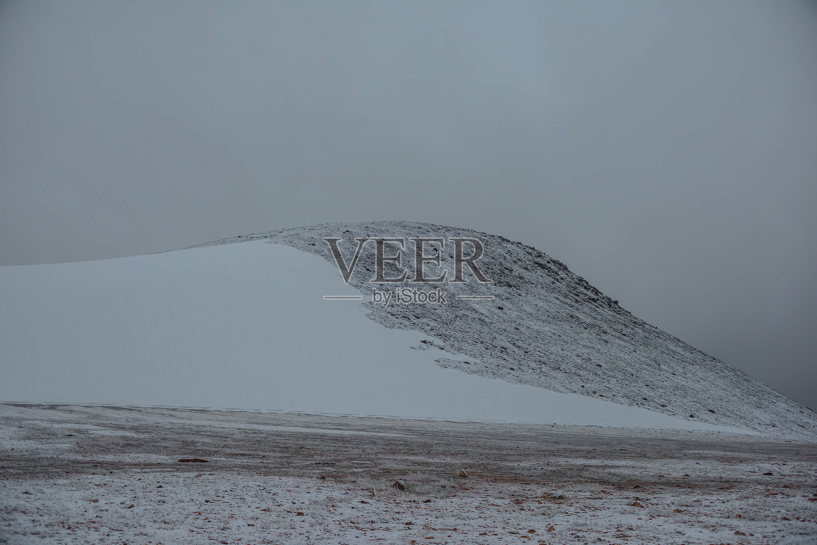 雪覆盖的石头小道上，锋利的石头和冰冻的草丛映衬着多云天气下的雪山。高山中新近降雪的雾气弥漫，形成了大气的迷雾景观。被雪封住的山谷。照片摄影图片