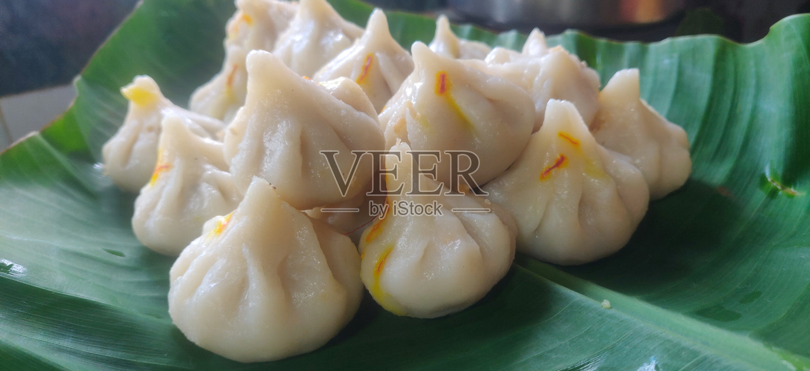 马哈拉施特拉的甜点莫达克，供奉给甘尼什神，上面撒有藏红花，旁边有一碗酥油，背景是甘尼什神像。照片摄影图片