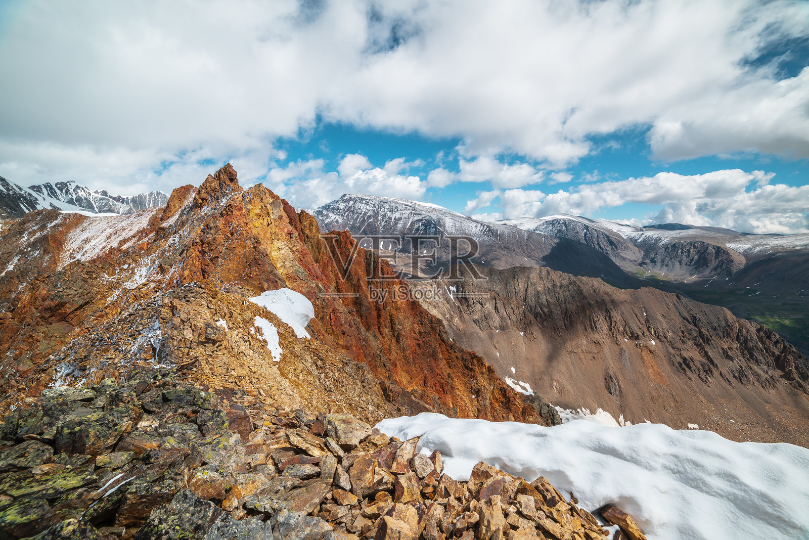阳光下生动锐利的山巅。闪亮的金色尖峰。色彩斑斓的红色岩石山顶。高山上新落的雪。阳光明媚的多云阿尔卑斯风景。石质山脊上的雪堆。照片摄影图片