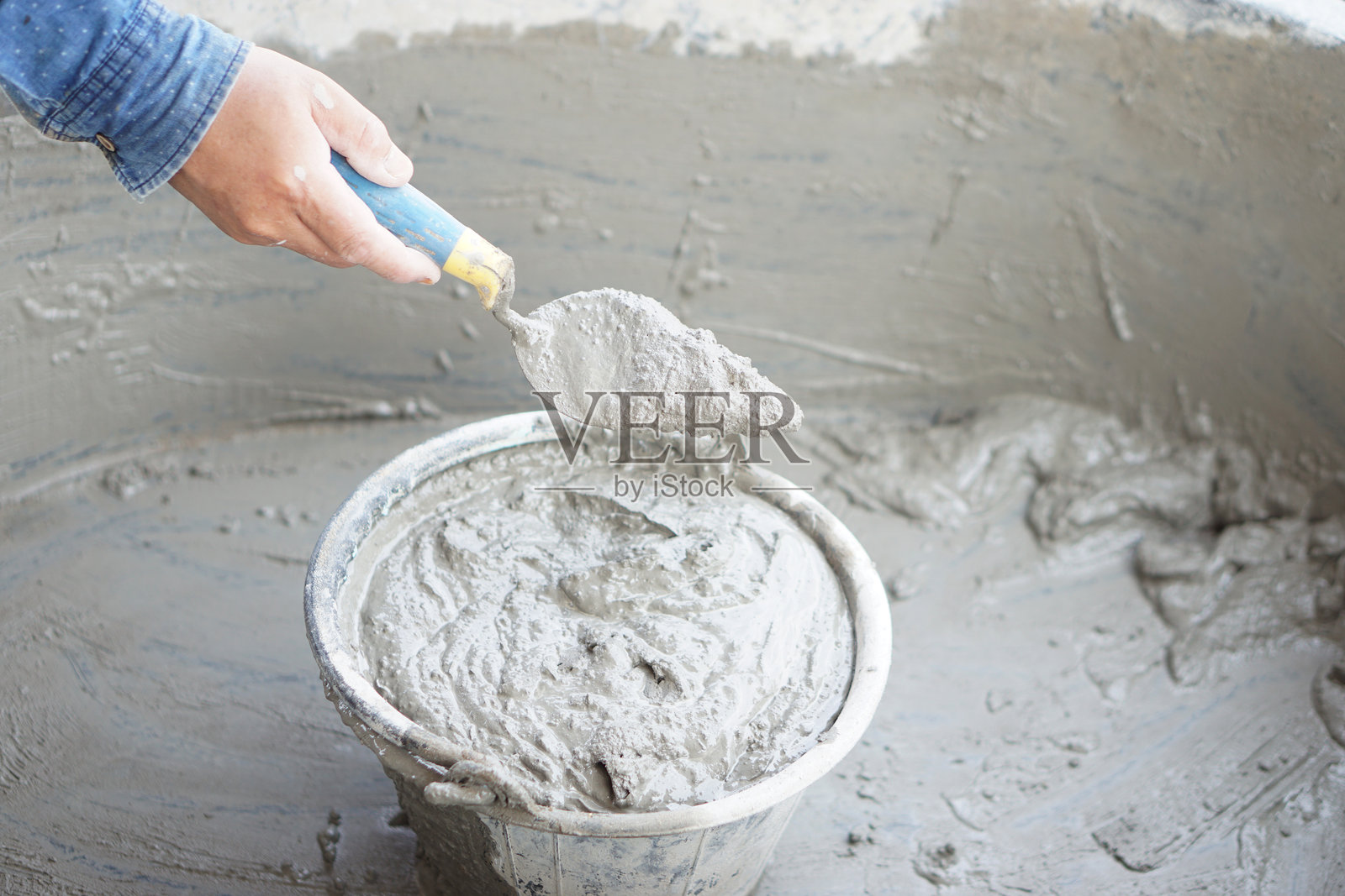 工人手持抹子在桶中搅拌湿水泥的特写。概念：建筑工作。水泥施工过程。选择优质和合适的建筑材料产品。照片摄影图片