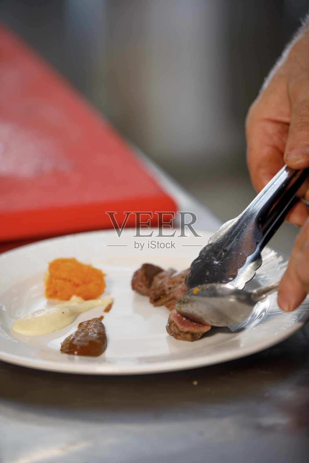 厨师正在准备一道包含肉类、各种酱汁和南瓜的菜肴。照片摄影图片