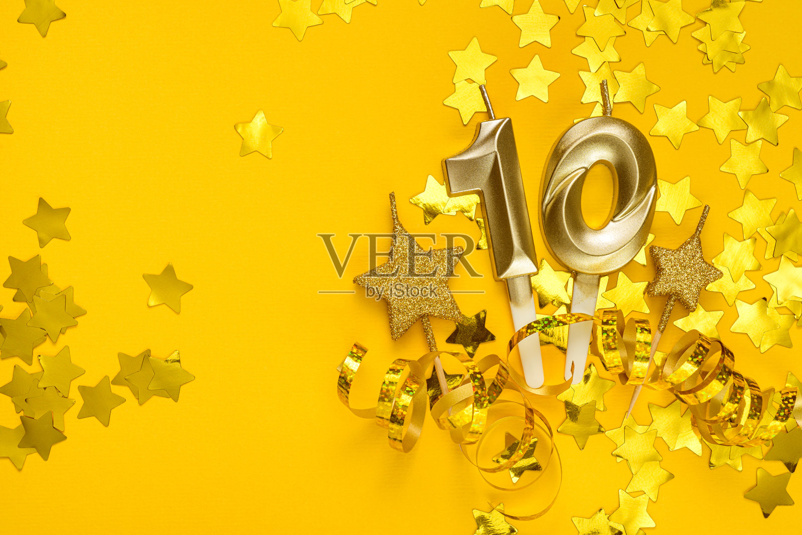 黄色背景上有金色的数字十蜡烛，周围环绕着星星彩纸和彩带。照片摄影图片