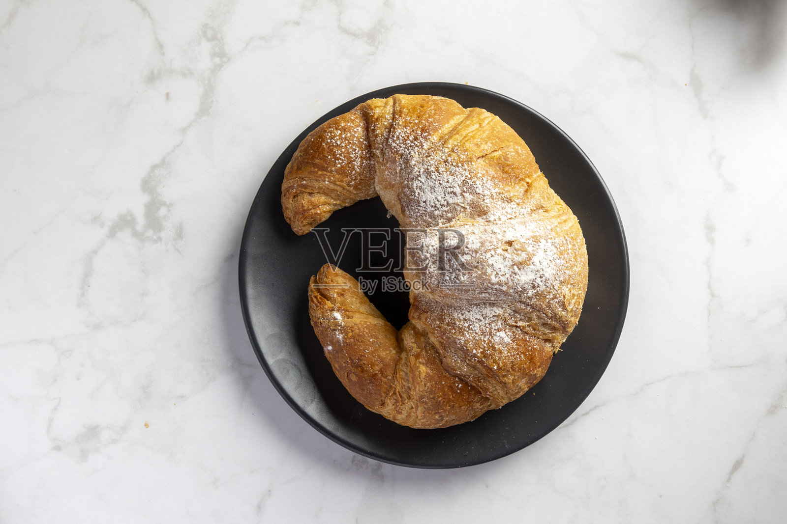 黑色盘子上的粉状可颂，背景为大理石纹理。照片摄影图片