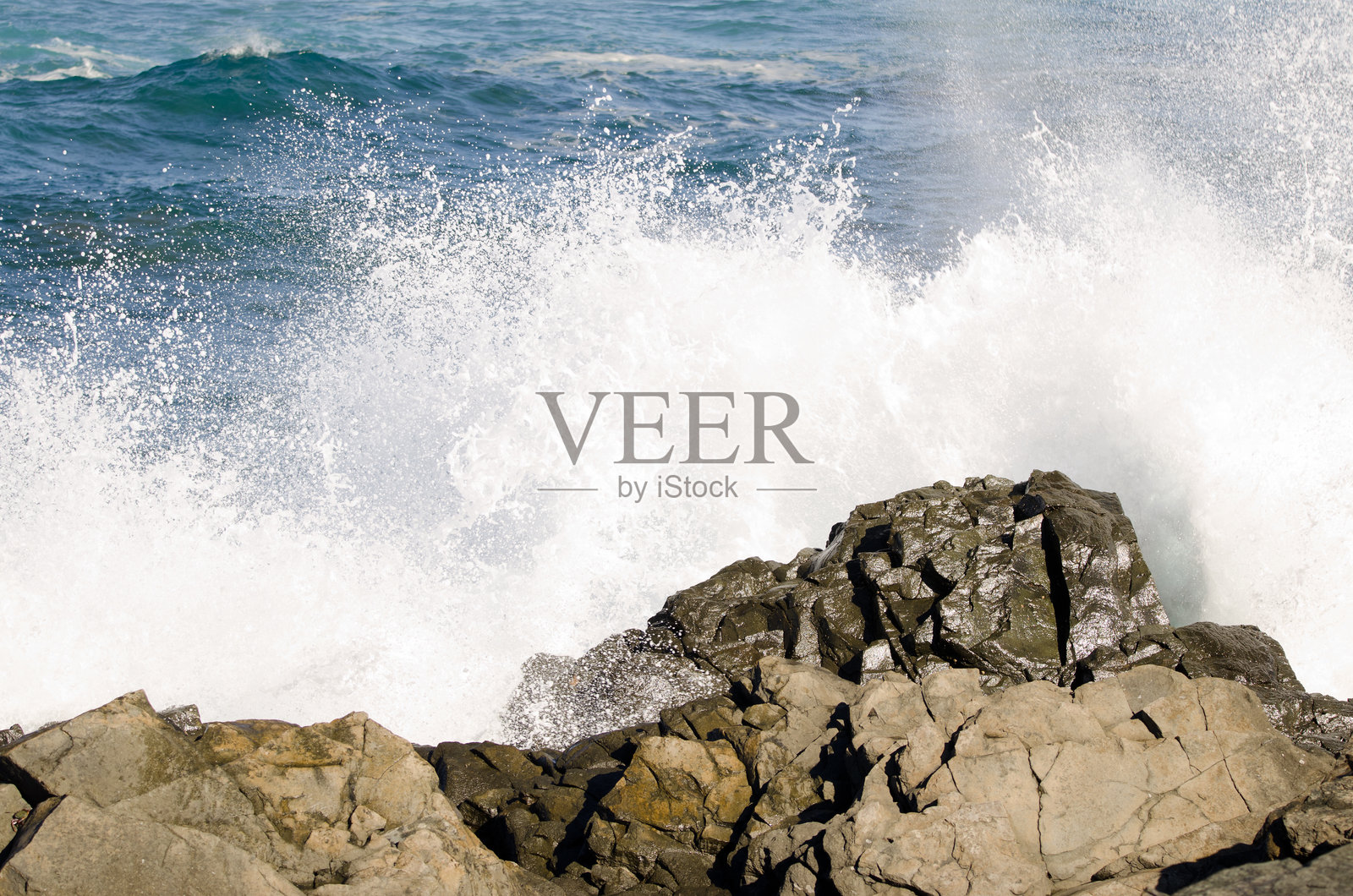 海浪拍打海岸岩石的溅起水花。照片摄影图片