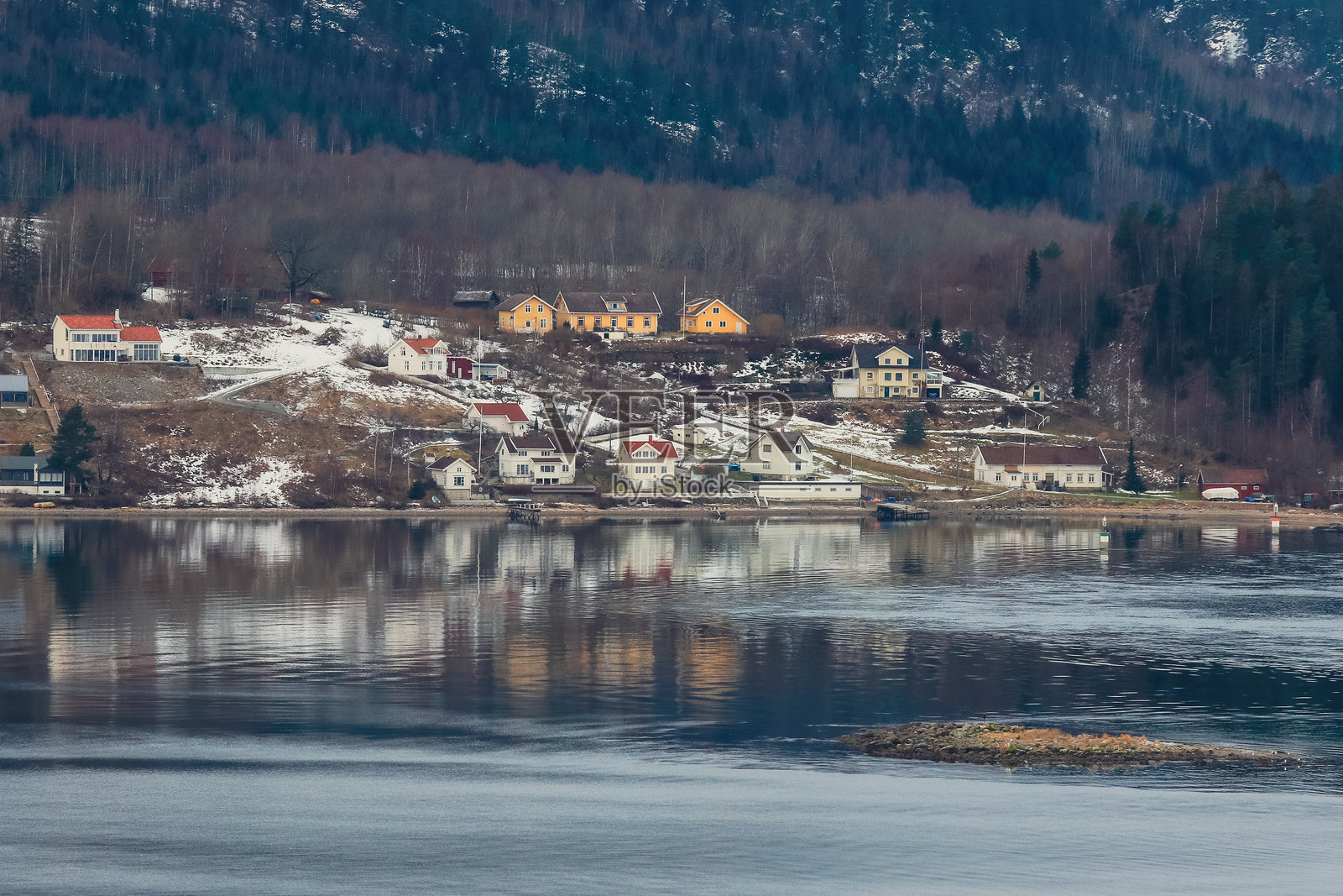 冬季宁静的挪威村庄风景，坐落在水边，背景是被雪覆盖的山丘。照片摄影图片