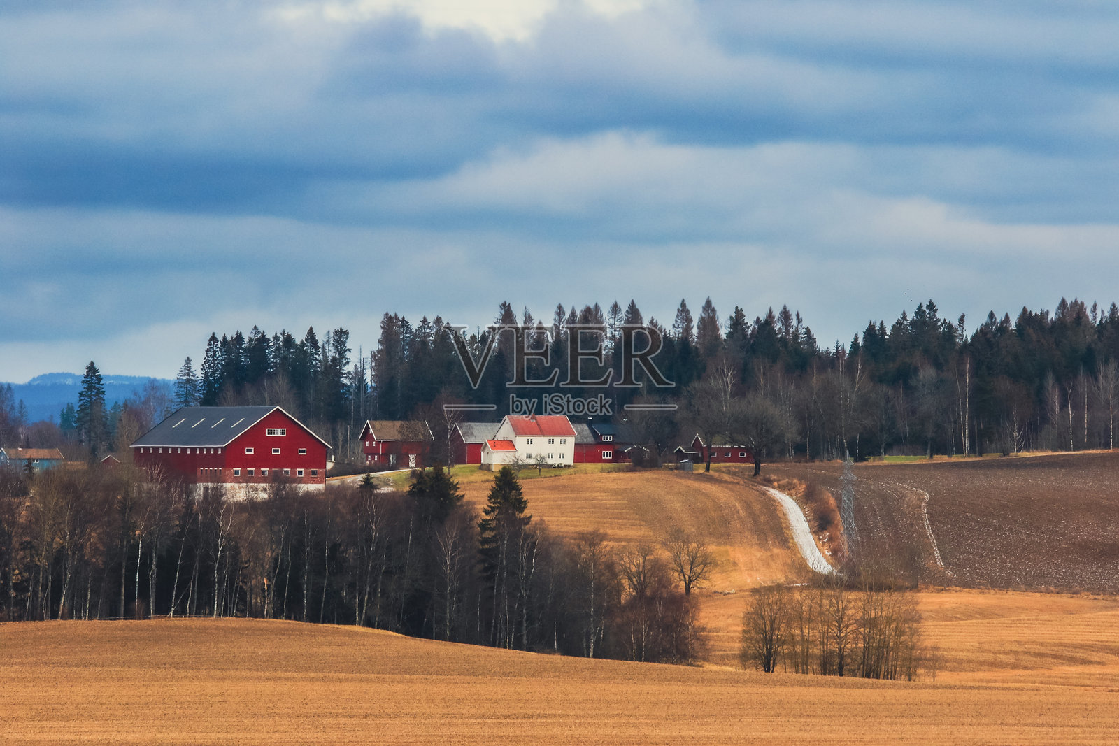 风景如画的挪威乡村，传统的红色农舍和起伏的田野在戏剧性的天空下交相辉映照片摄影图片