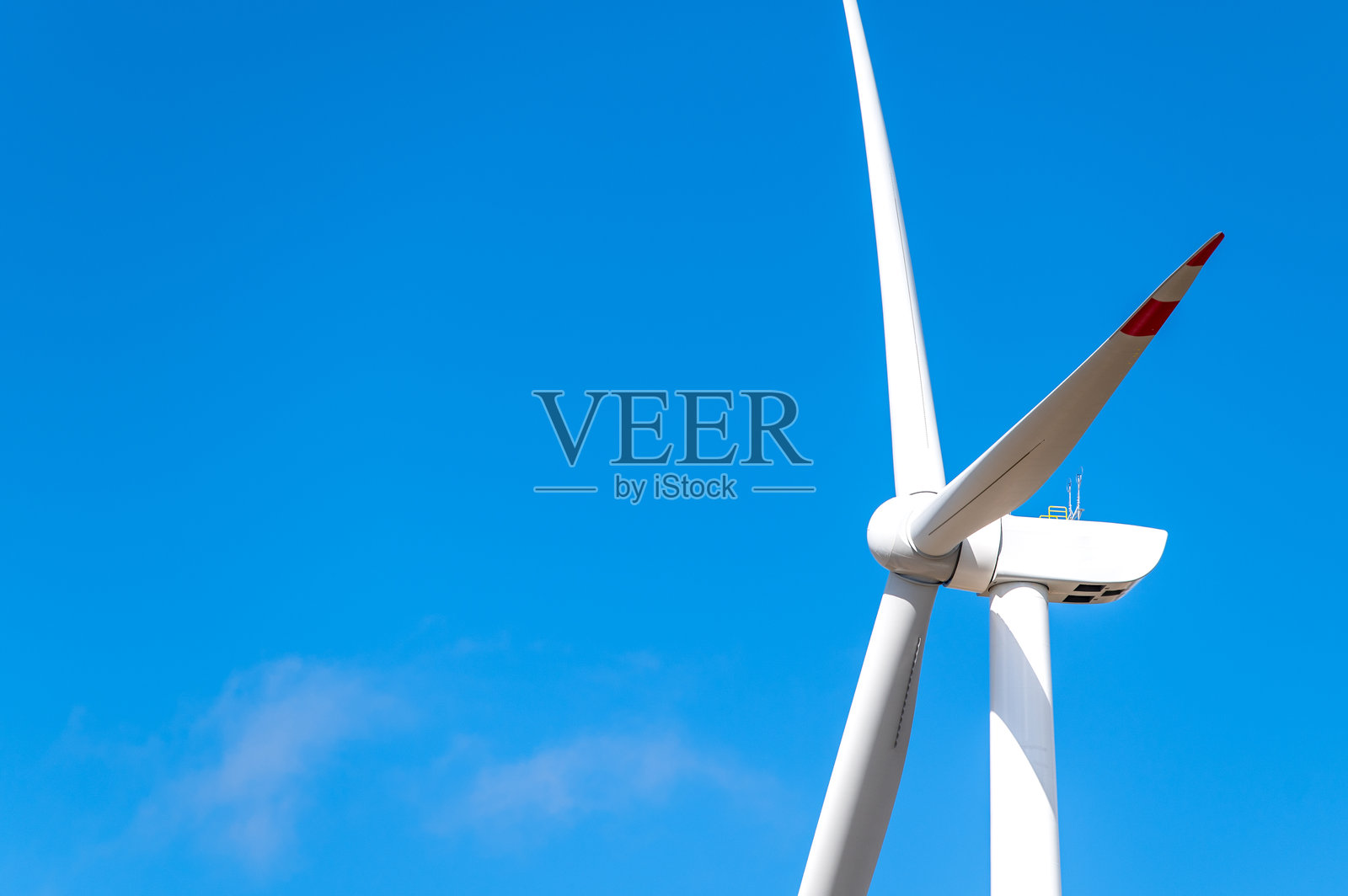 一座现代风力涡轮机在晴朗的蓝天和几朵白云的映衬下高高耸立。照片摄影图片