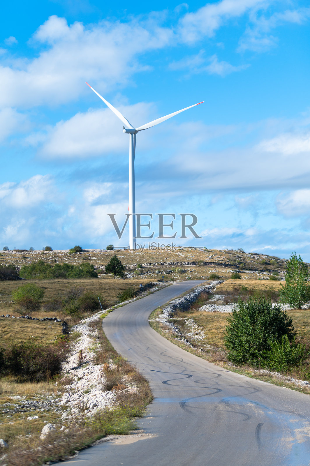 一座现代风力涡轮机在晴朗的蓝天和几朵白云的映衬下高高耸立。照片摄影图片