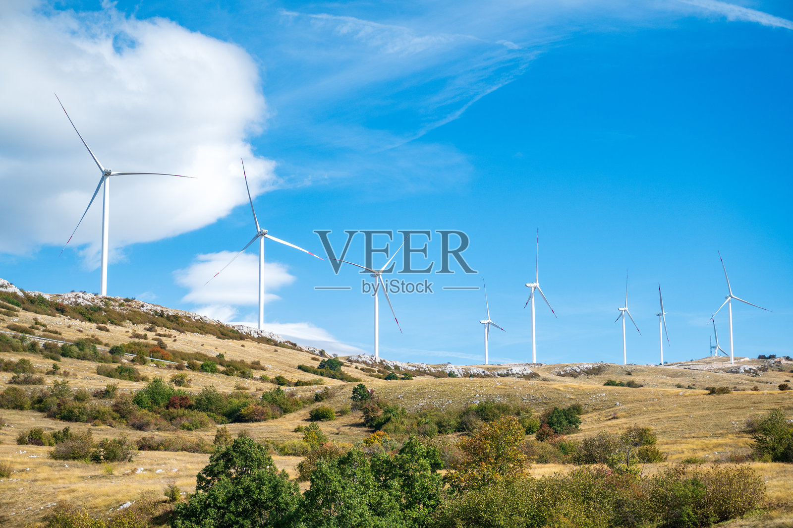 一座现代风力涡轮机在晴朗的蓝天和几朵白云的映衬下高高耸立。照片摄影图片