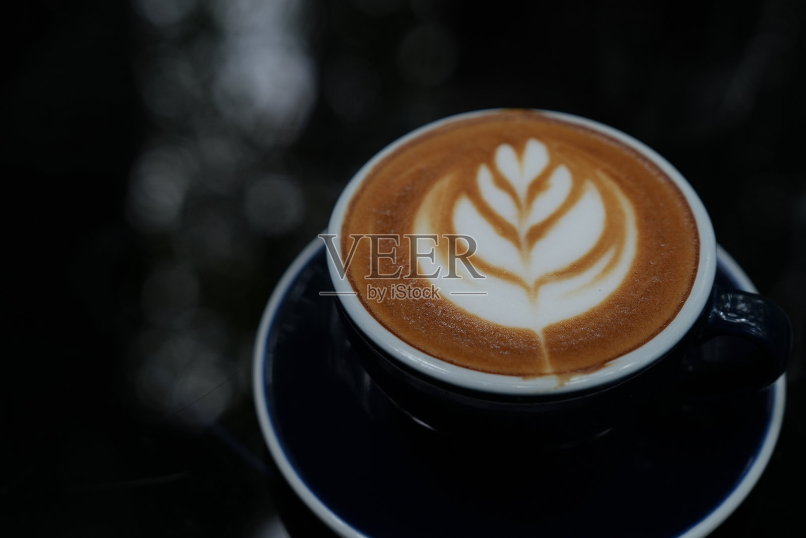 黑色背景下的玻璃杯热咖啡拿铁，上面有拉花奶泡。照片摄影图片