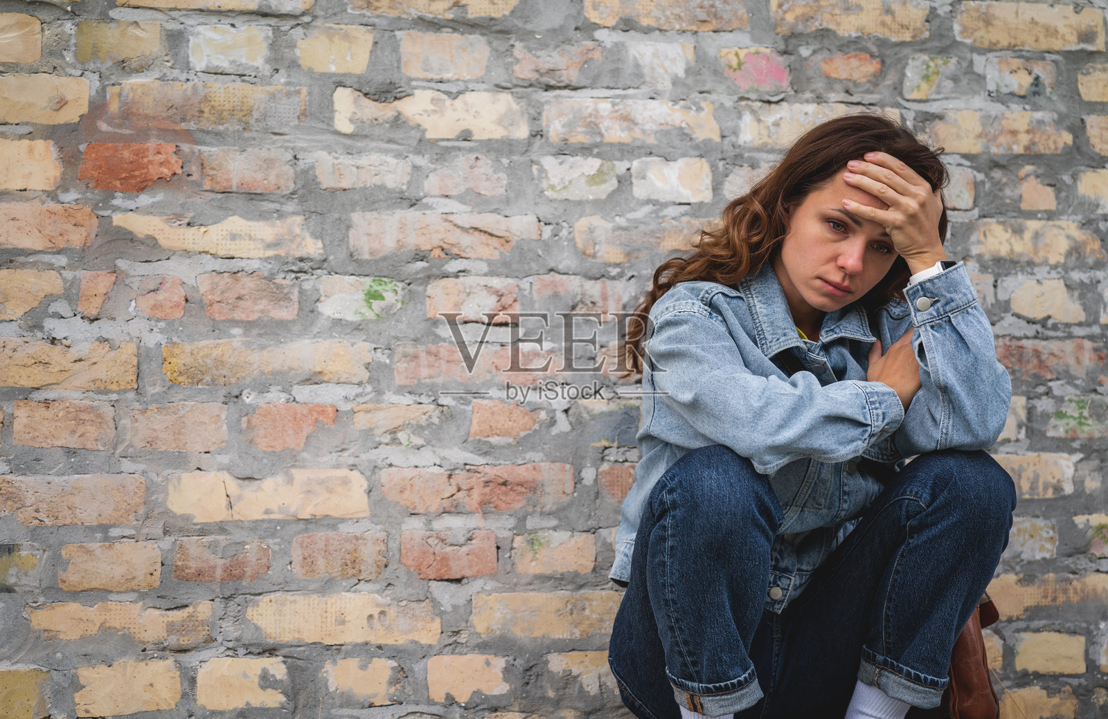孤独、压力大且疲惫的城市女性坐在街道上的砖墙旁。照片摄影图片
