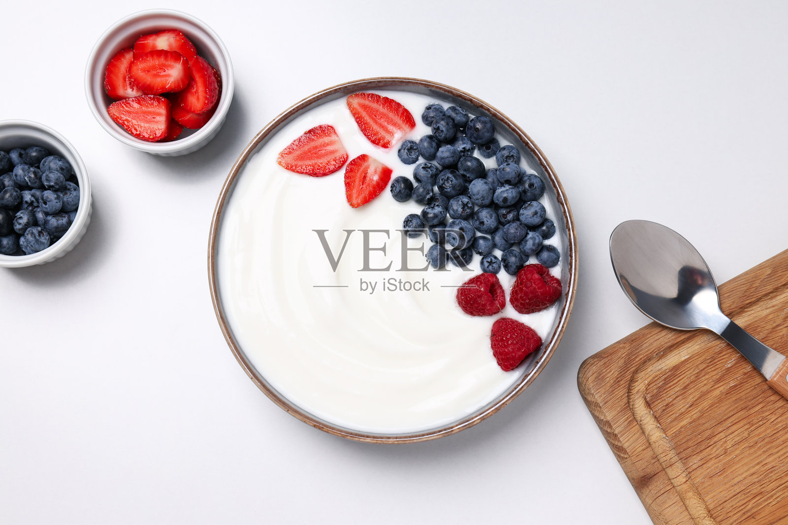 白色背景上的碗里装有酸奶和浆果，旁边有勺子和砧板，俯视图照片摄影图片