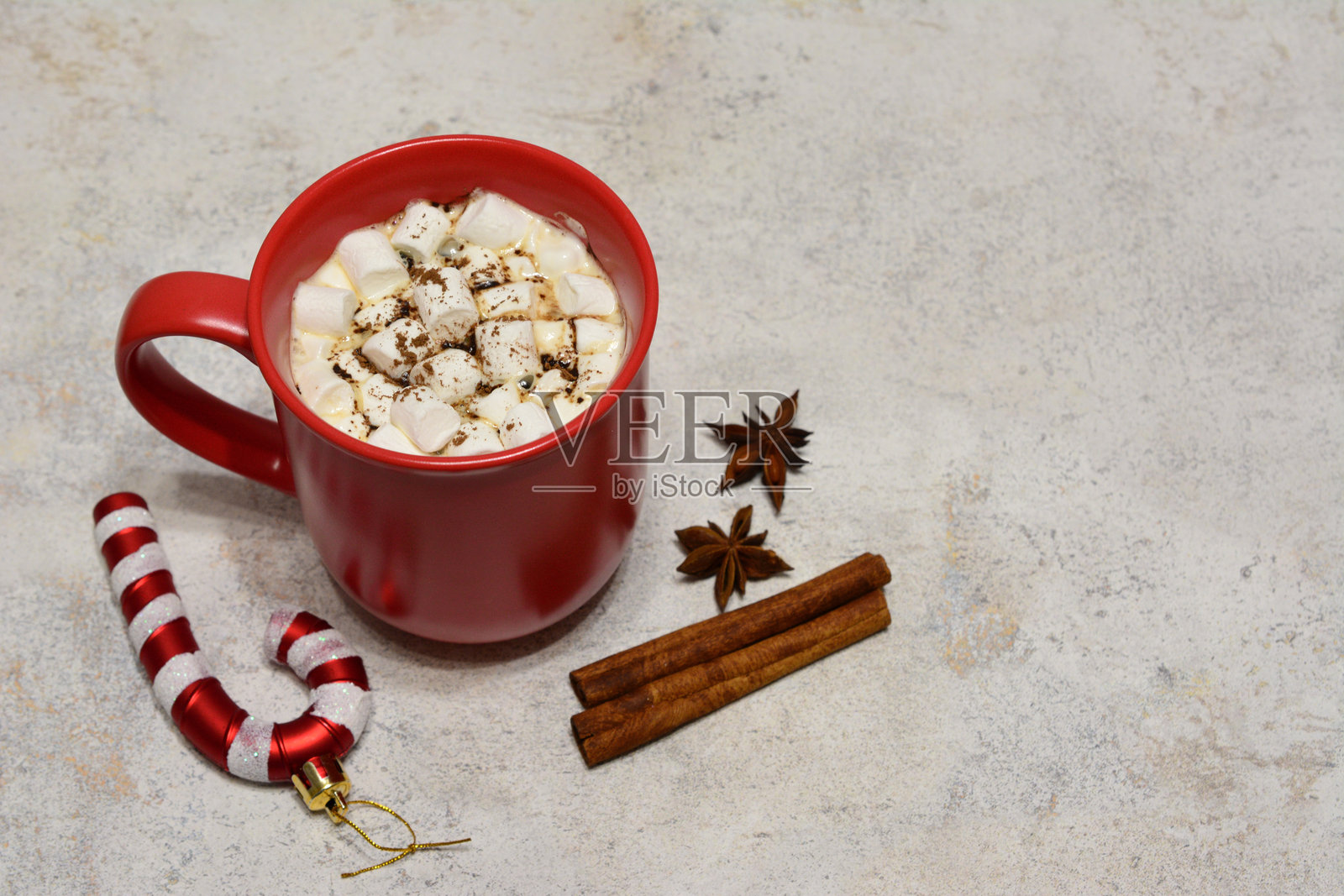一只红色的马克杯里装着棉花糖和一根糖果手杖，背景是灰色的。照片摄影图片