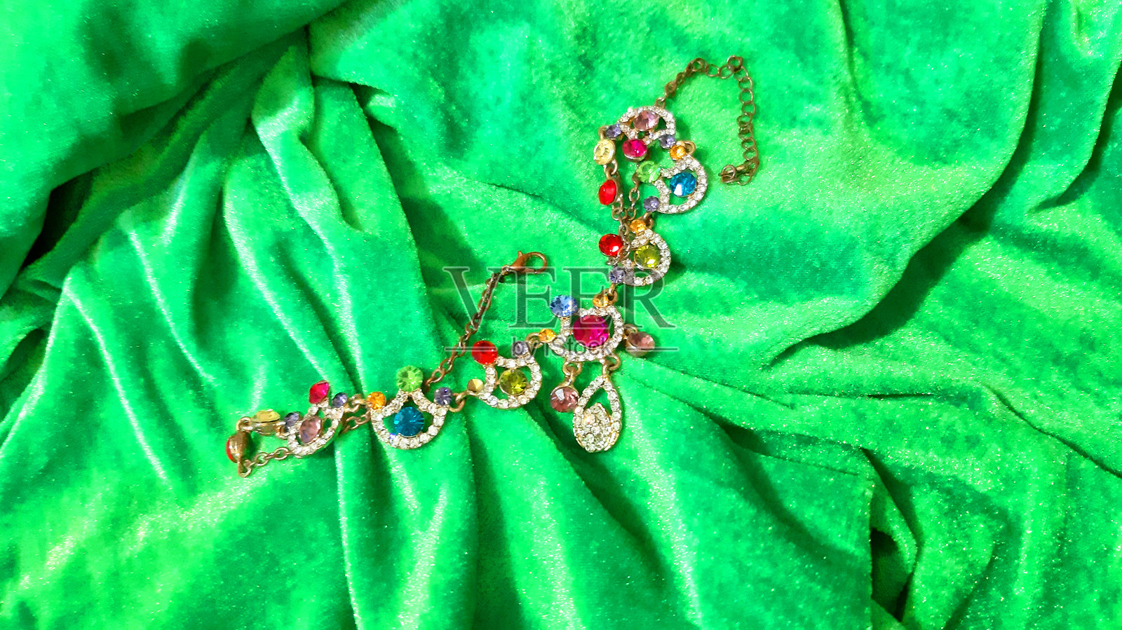 女性金色珠宝，镶嵌多彩宝石，背景为明亮的绿色。背景设计，摄影新颖。纺织品，面料模板，现代照片。照片摄影图片