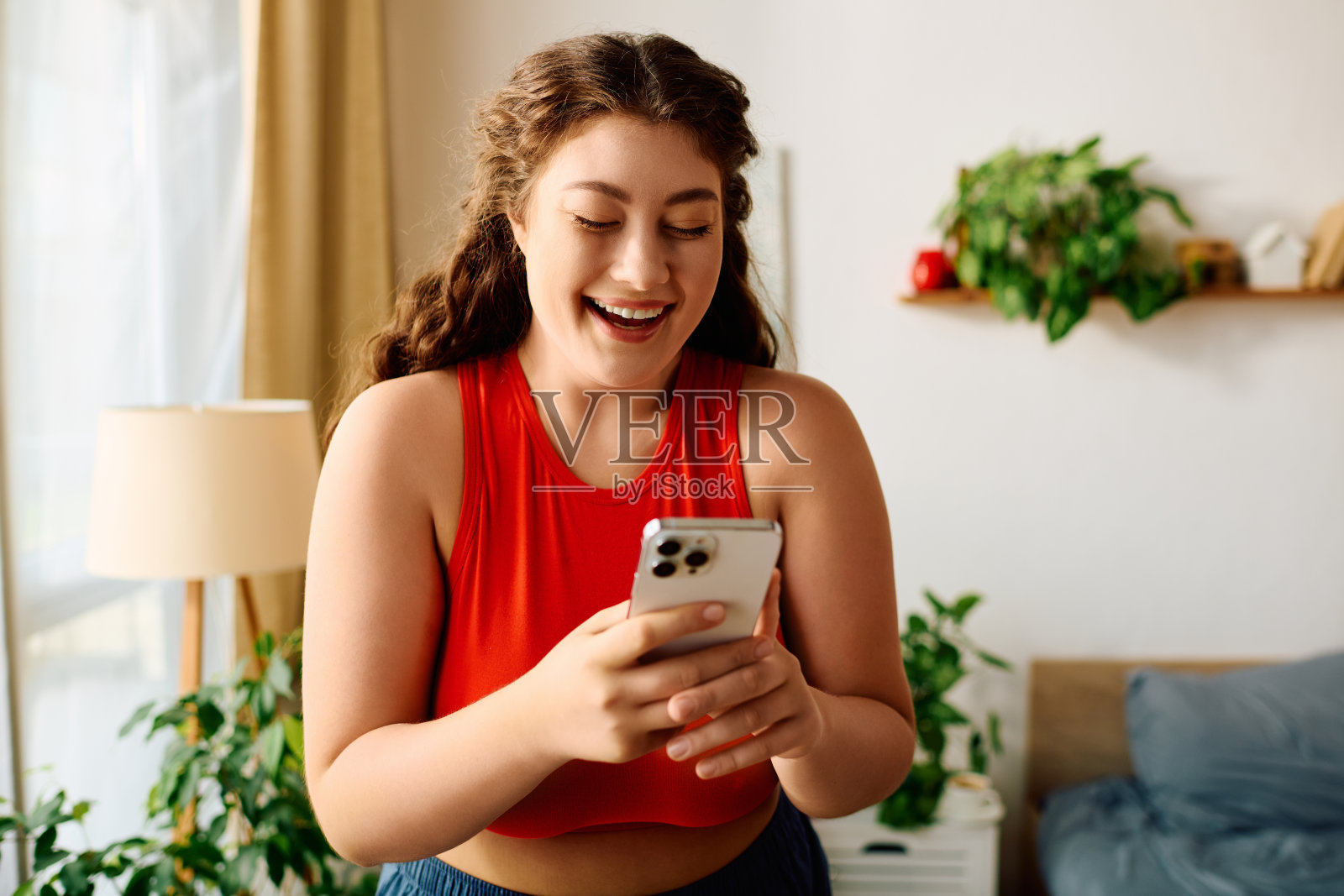 一位卷发的年轻女子一边笑一边在家里玩手机照片摄影图片