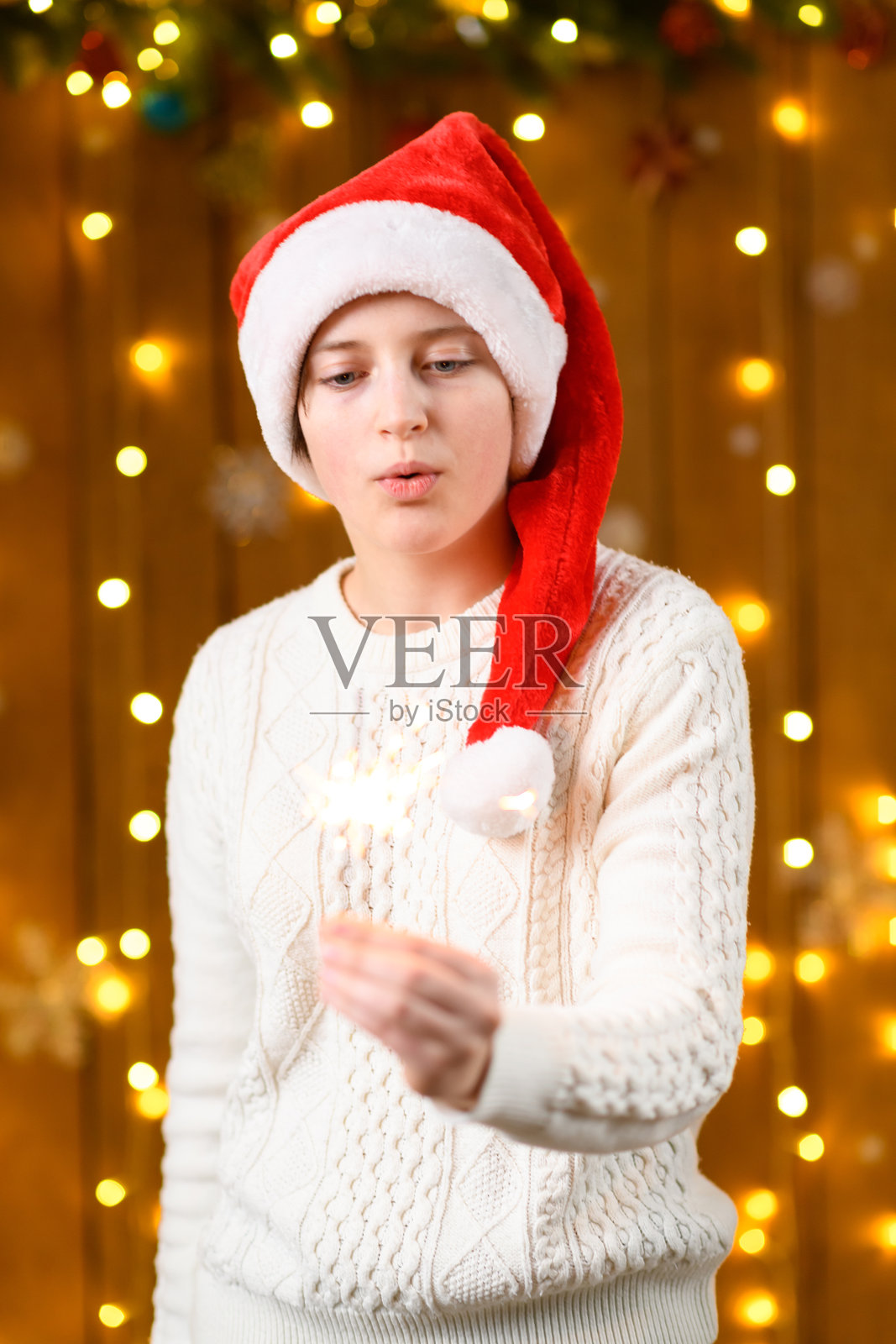 一个少女手持烟花棒，身边是新年节日装饰、节日灯光和花环。照片摄影图片