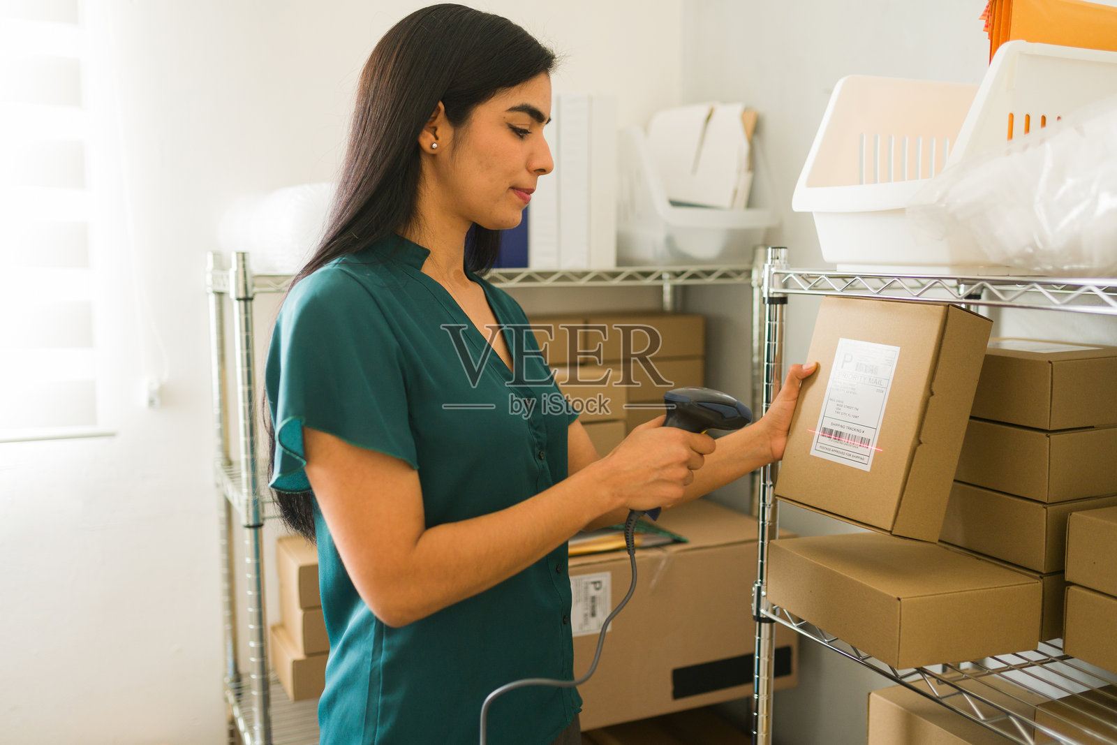 女性企业家使用条形码扫描器在电子商务仓库中整理包裹，代表小型企业运营和库存管理。照片摄影图片
