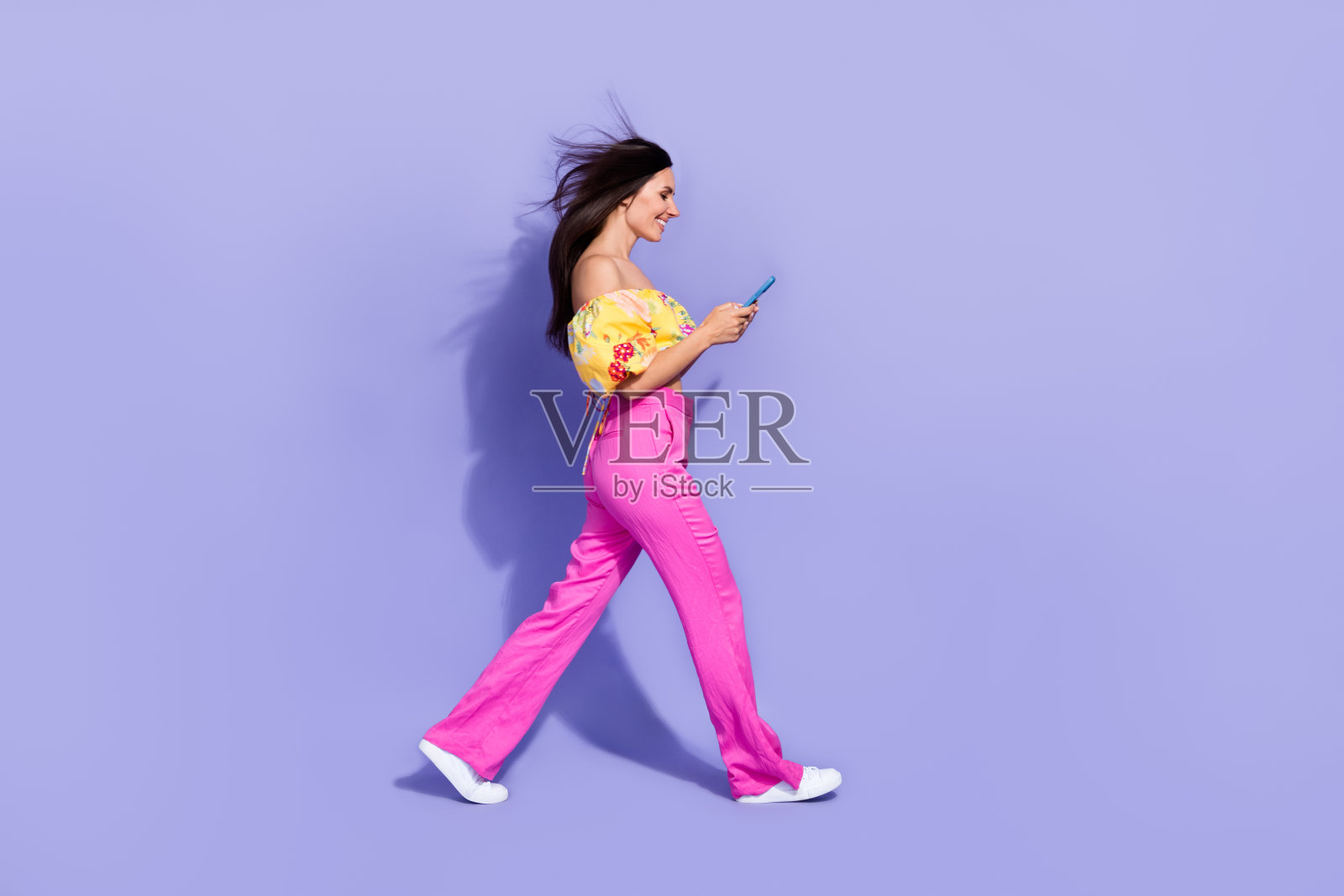 全身侧面照，迷人的人拿着电话走在紫色背景上。照片摄影图片