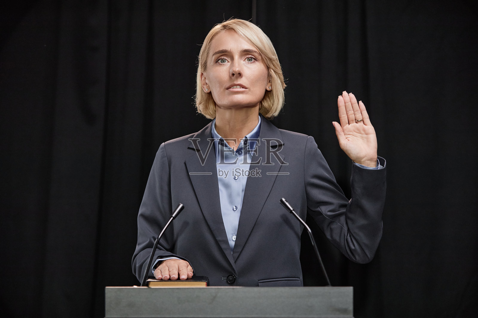 女性政治家身穿西装，举手宣誓遵守法律，站在室内讲台前。照片摄影图片