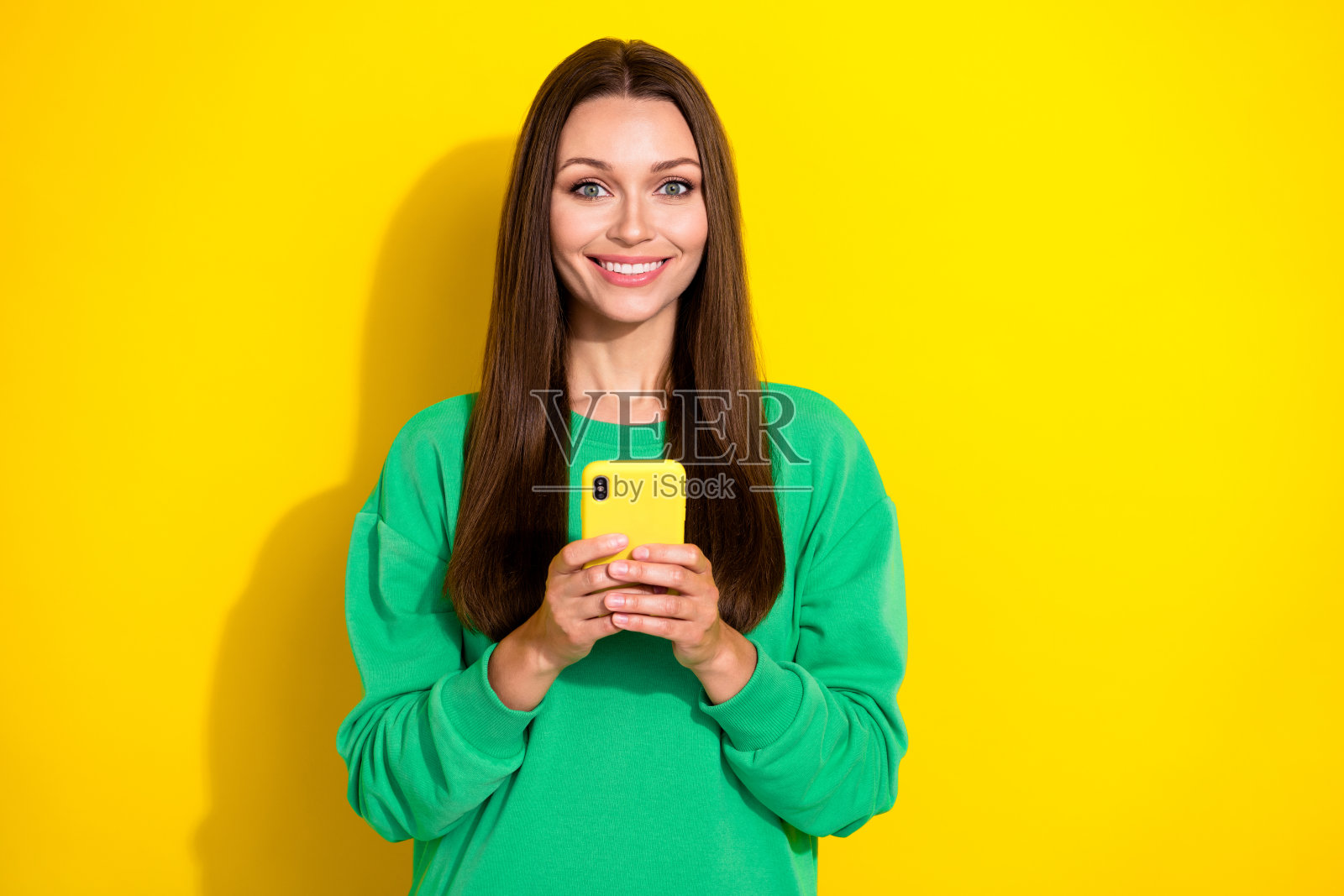 迷人的年轻女士在黄色背景下穿着时尚的绿色运动服，手持电话与朋友聊天的照片肖像照片摄影图片