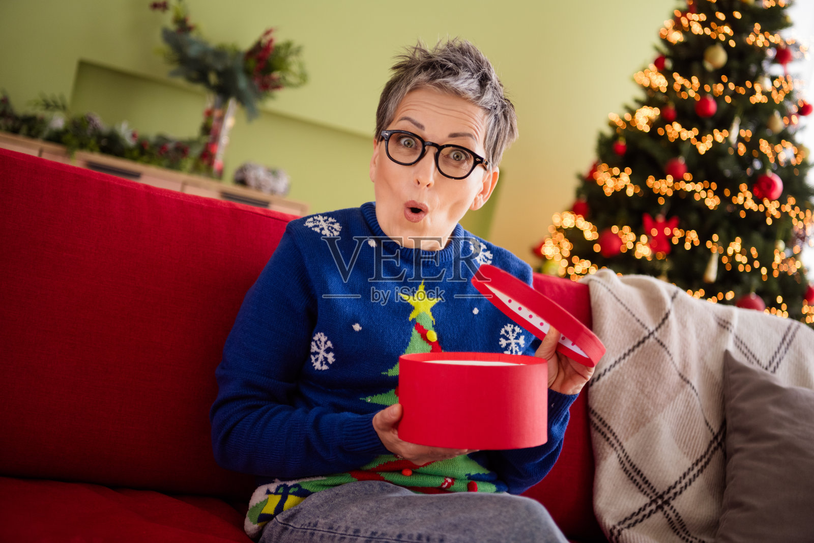 快乐兴奋的女性穿着蓝色毛衣，在温馨的室内气氛中打开圣诞礼物，感受新年的魔力。照片摄影图片