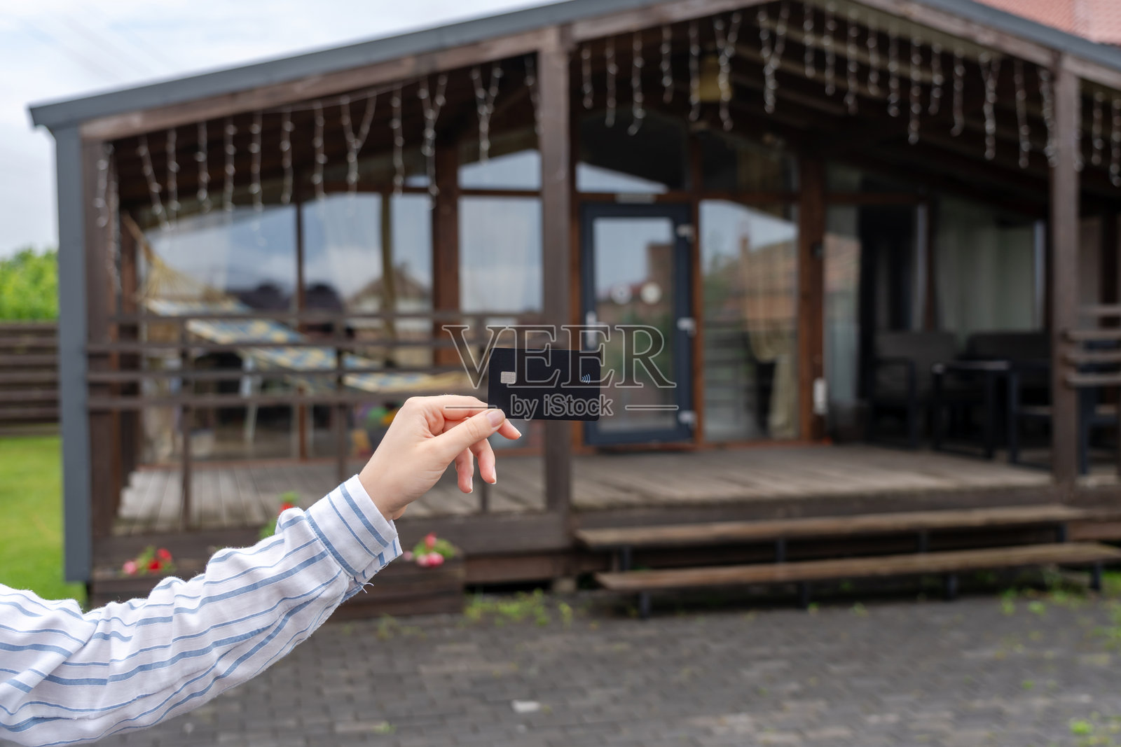 手握塑料信用卡，背景是新房子。经纪人、抵押贷款、物业、房地产概念。购买或租赁。照片摄影图片