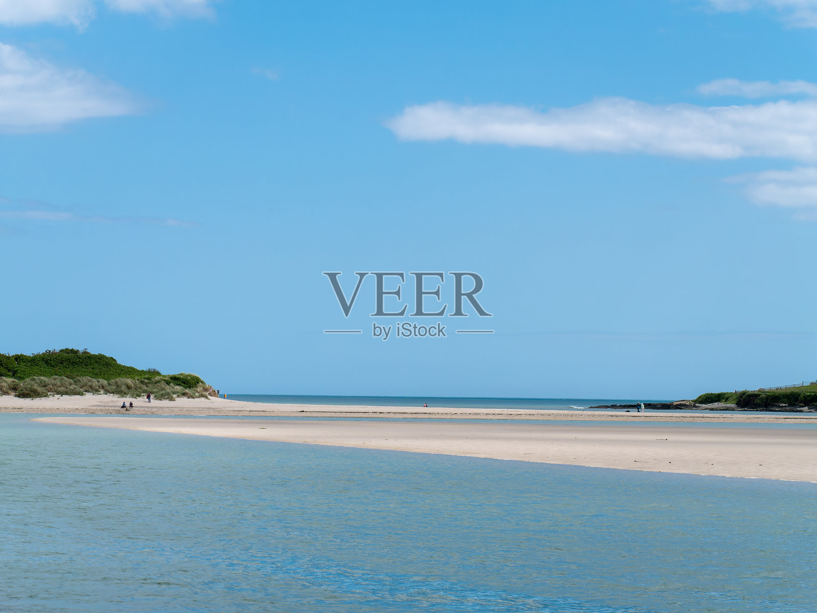 晴朗的天空下，美丽的沙滩上有几个人。爱尔兰夏日的如画海景。留白空间。人们在沙滩上散步。照片摄影图片