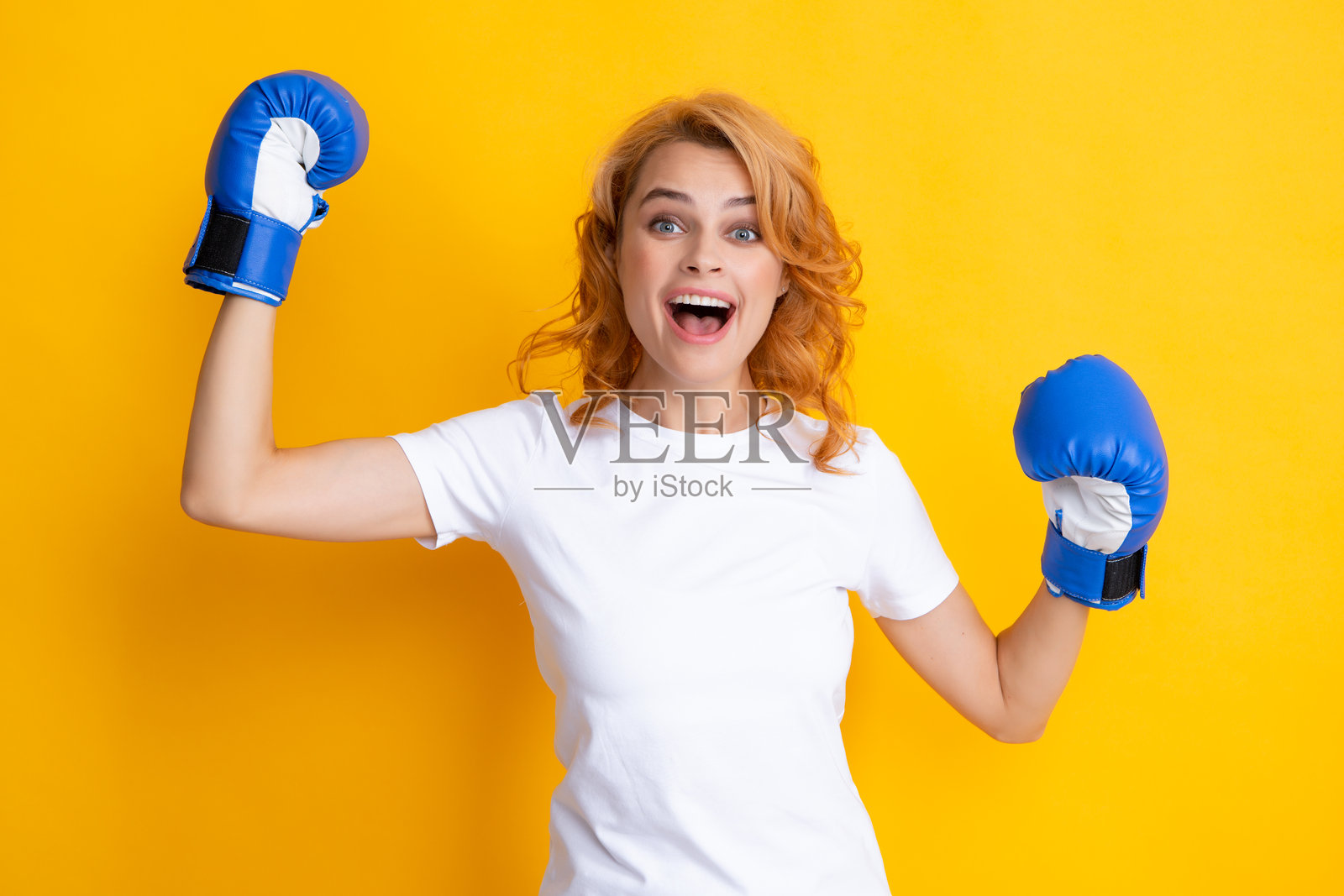欢快的女性庆祝胜利。获胜的女性拳击手，背景为黄色。兴奋的获胜女性佩戴拳击手套。成功力量女性的概念。女孩为成功而战。照片摄影图片
