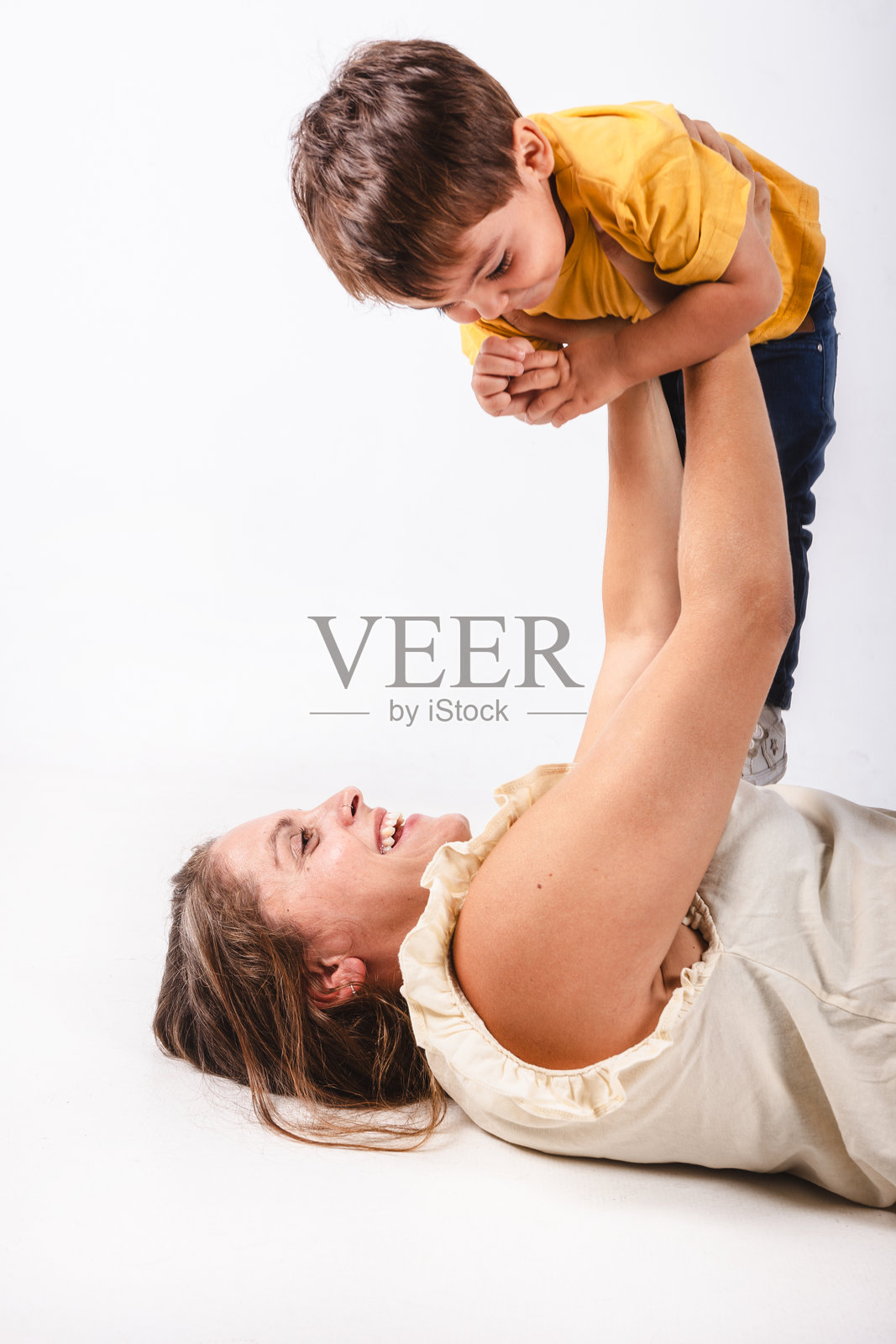 躺着的母亲愉快地玩耍，抱起她两岁的儿子。照片摄影图片