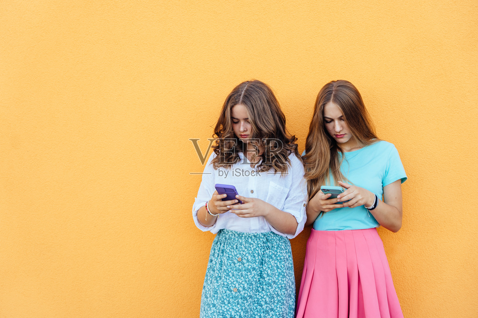 青春女孩在鲜艳的橙色背景下使用智能手机照片摄影图片