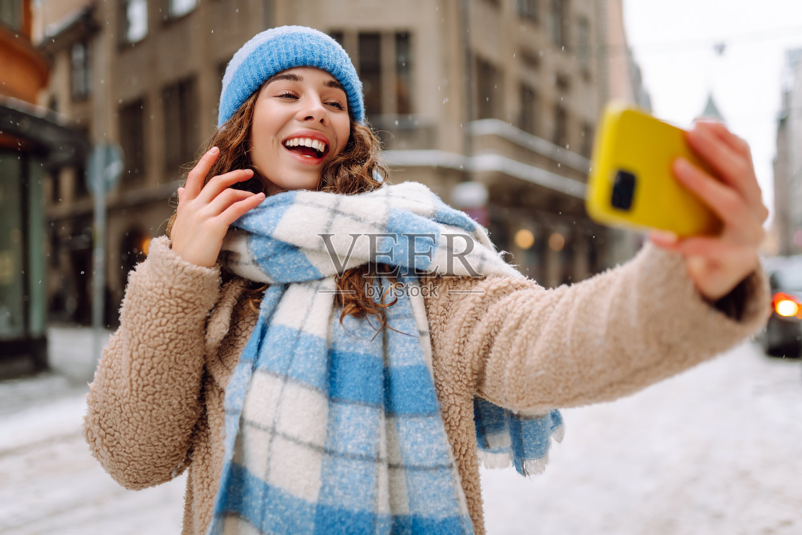 冬季街头，漂亮年轻女性在城市中散步时用手机自拍的户外生活肖像。照片摄影图片