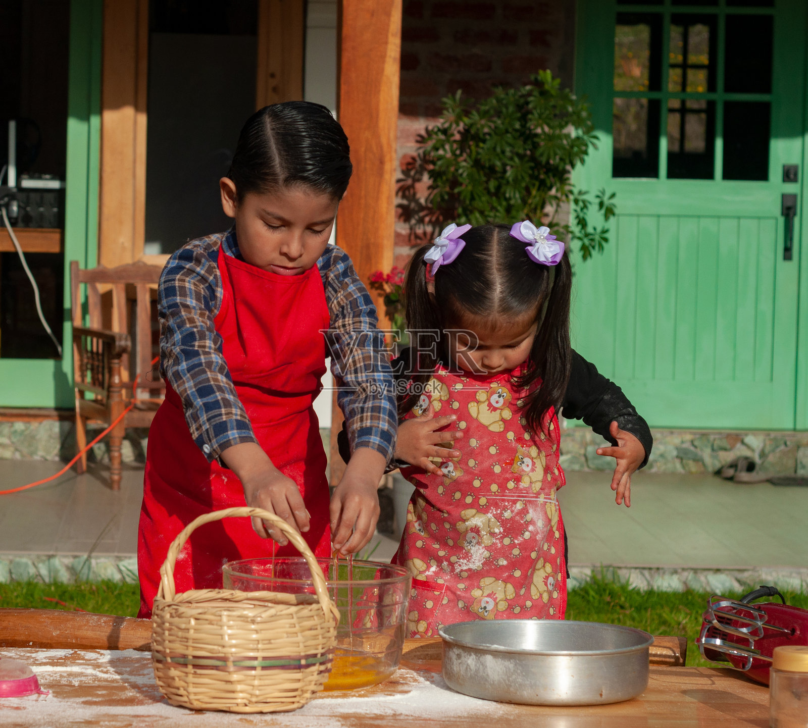 两个拉丁美洲儿童穿着围裙正在把鸡蛋打入一个木碗中照片摄影图片