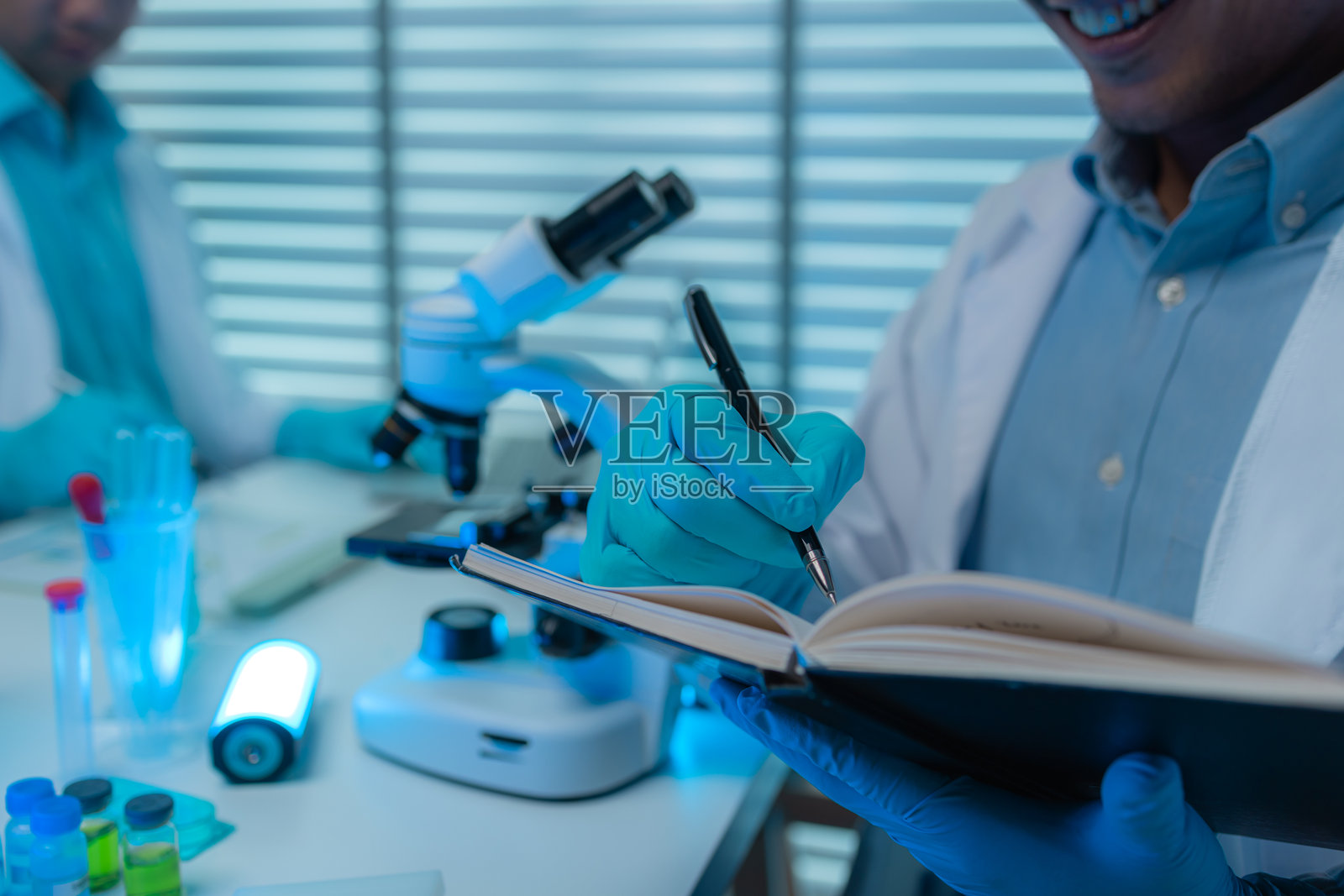 一位科学家在实验室中愉快地工作，一名科学研究人员正在进行他的项目，研究发现一种新的抗病毒公式，显微镜、报告、实验室和科学家的概念。照片摄影图片