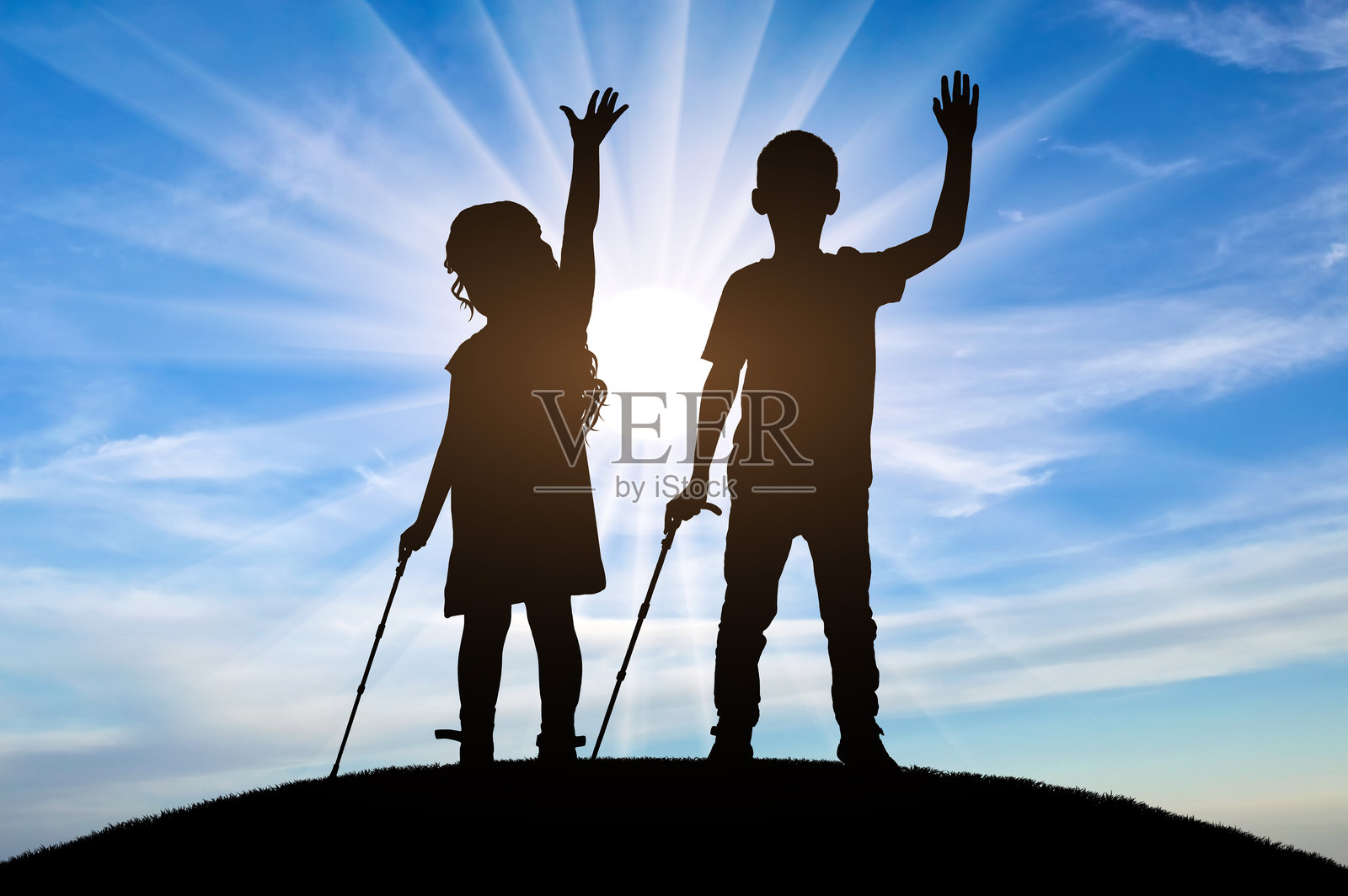 两个快乐的盲童的剪影，一个男孩和一个女孩站在山丘上，各自手持一根手杖。照片摄影图片