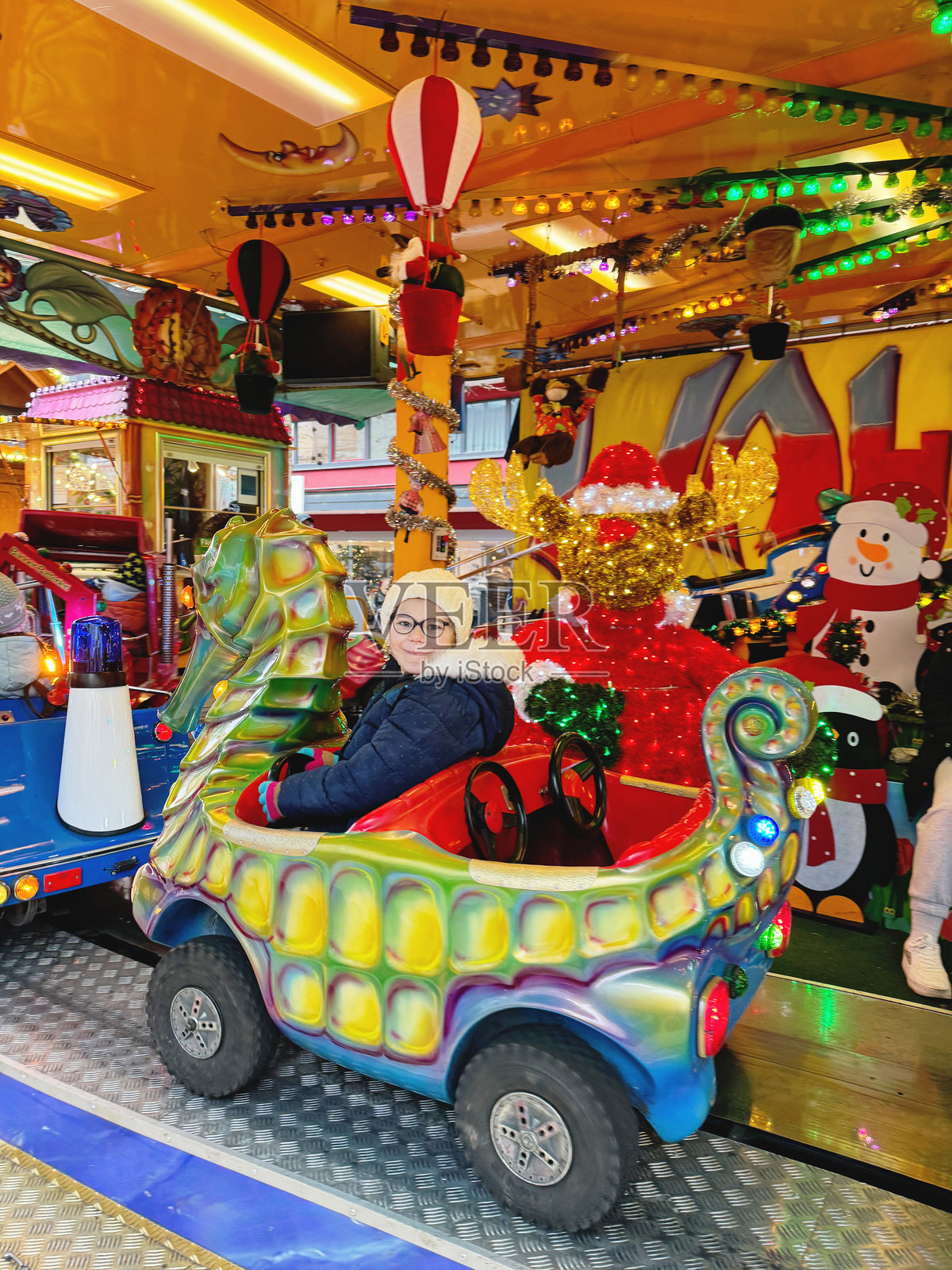 小女孩在圣诞游乐市场的旋转木马上骑行，户外场景。快乐的孩子在德国科隆的传统家庭圣诞市场上玩得很开心。照片摄影图片