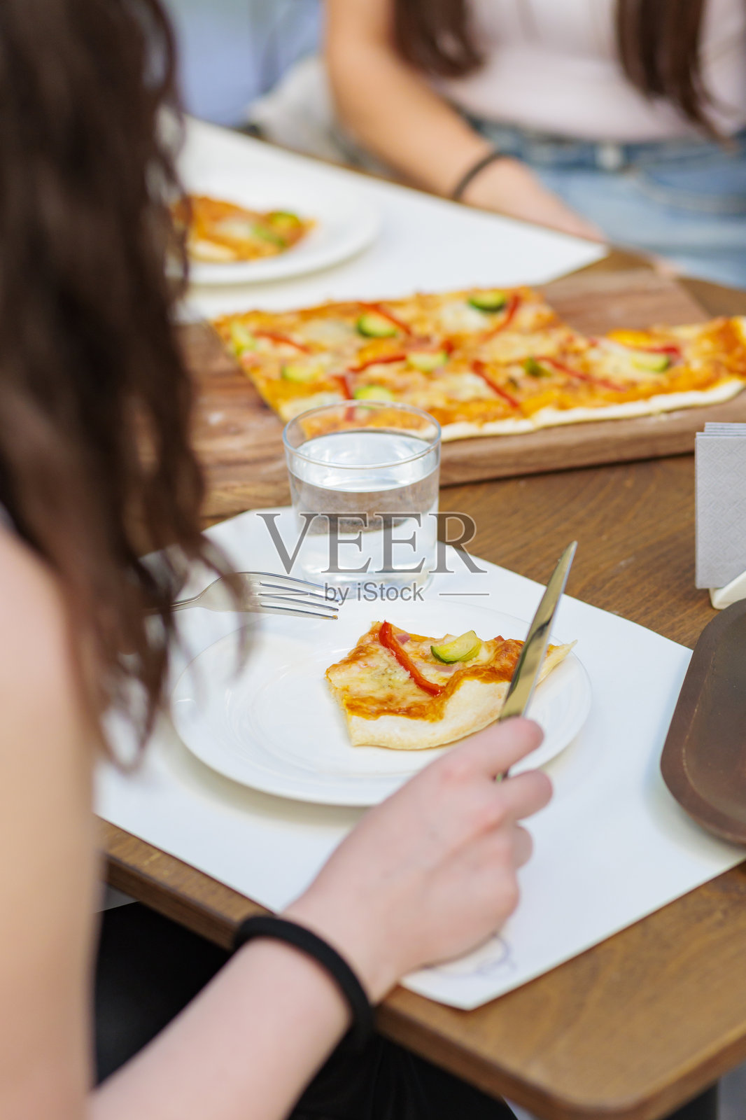 一个人在舒适的餐厅桌子上享用一片配有蔬菜的披萨，正值午餐时间。照片摄影图片