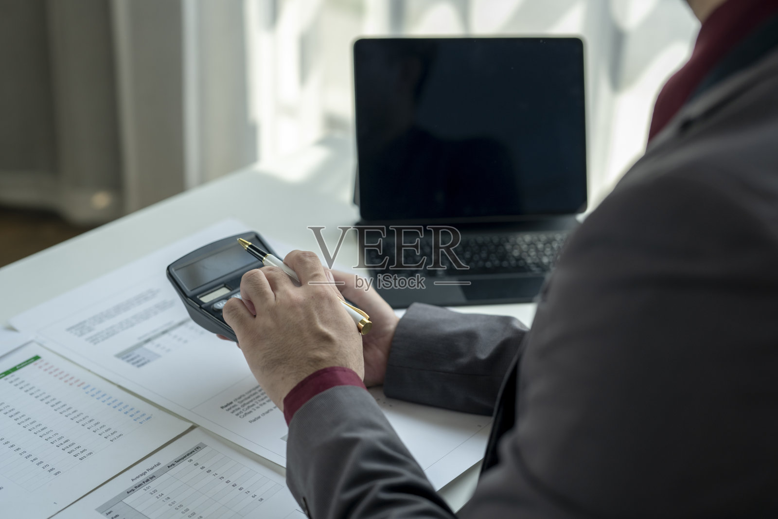 一名男子坐在桌子前，面前有一台计算器和一台笔记本电脑。照片摄影图片