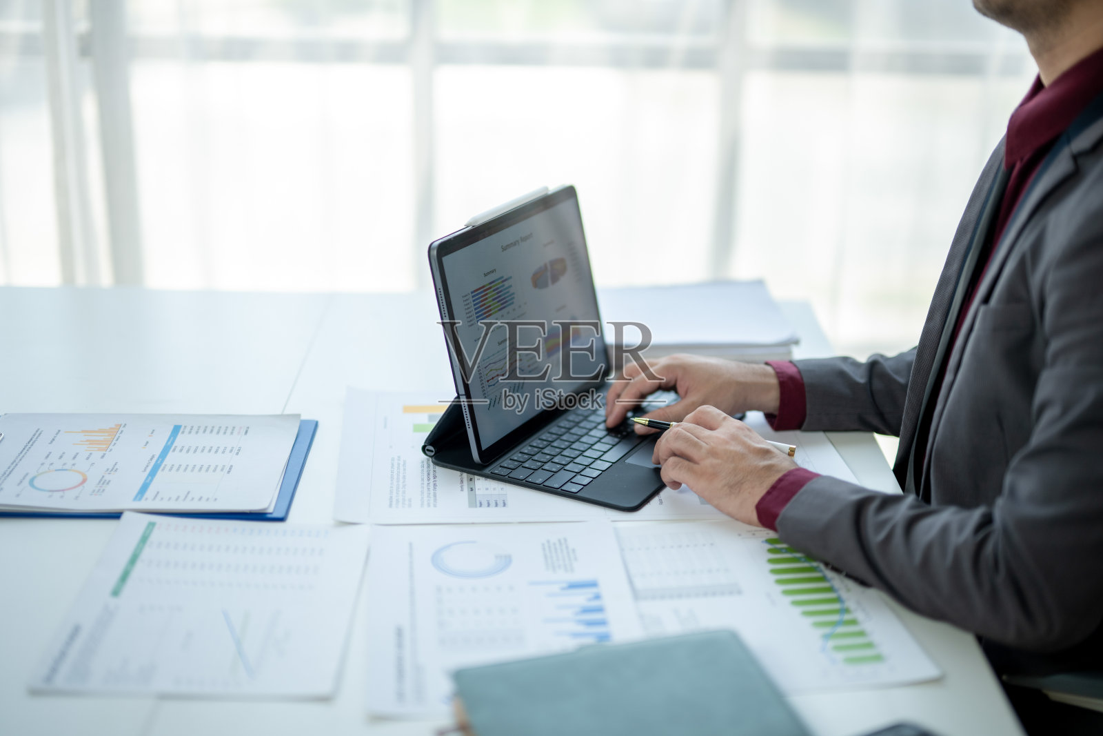 一名男子在桌子前使用笔记本电脑，桌上放着几份文件。照片摄影图片